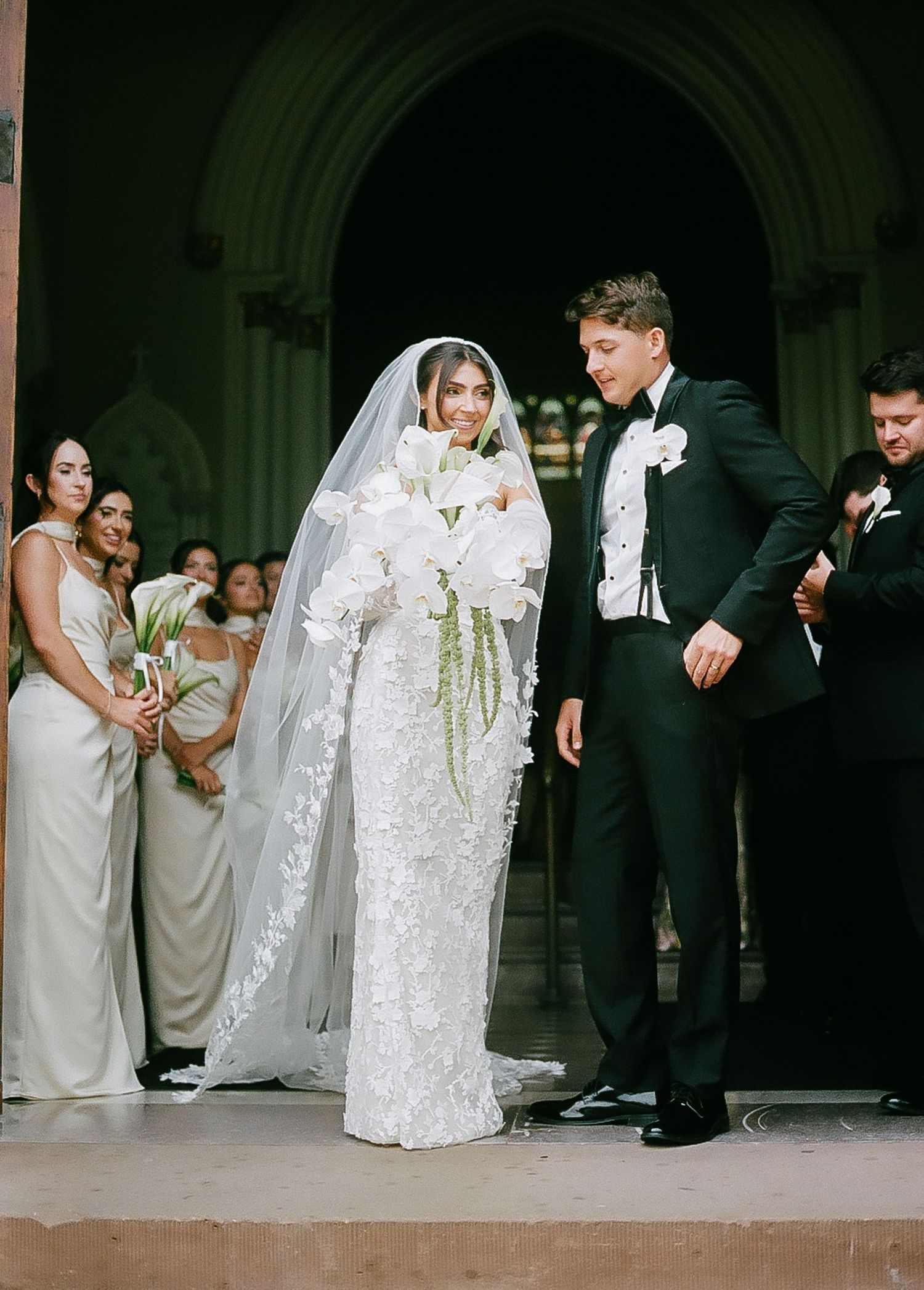 Bride and groom perform playful poses on stone steps outside a traditional architecture venue.