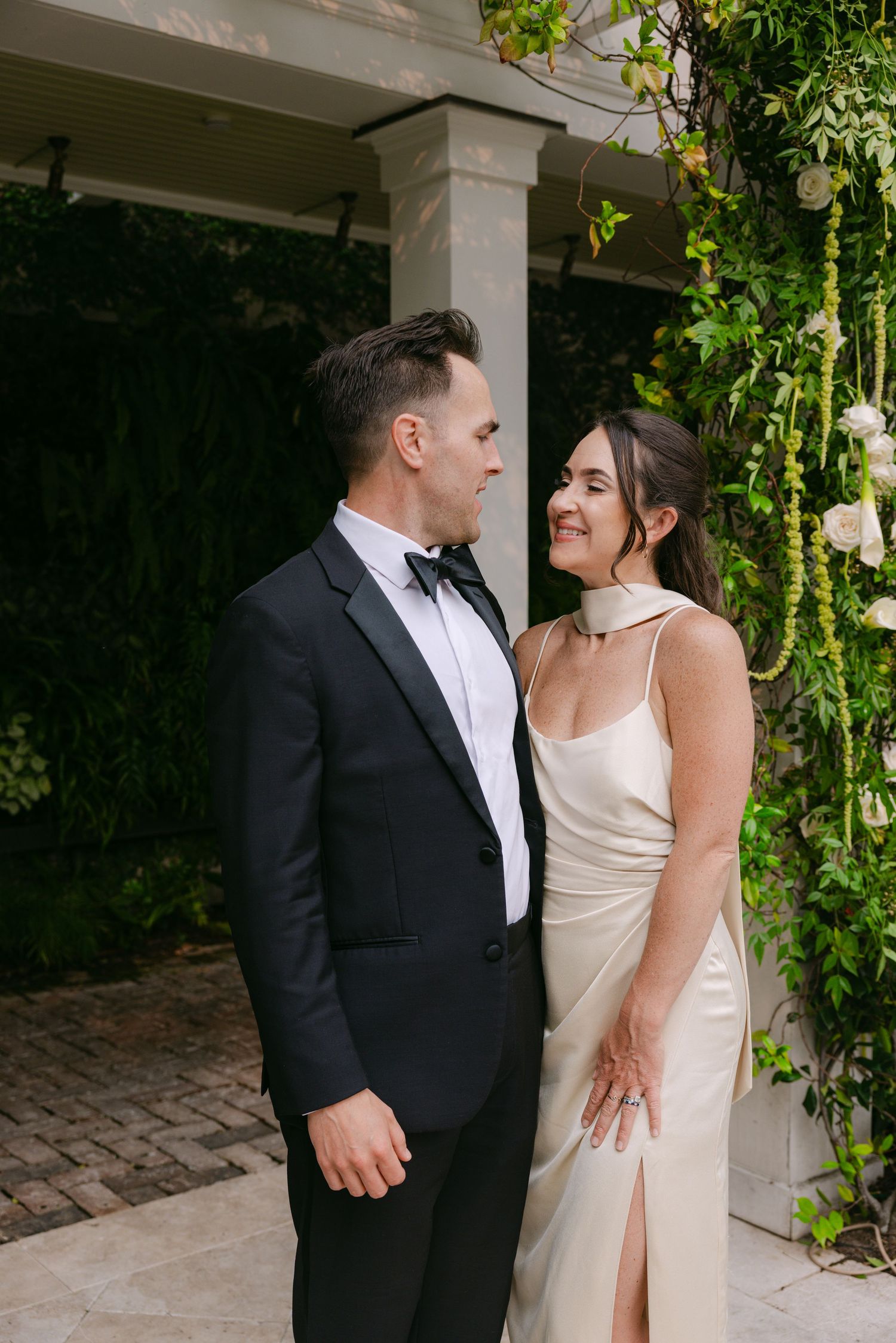 A couple shares an intimate moment under an archway covered in trailing vines and greenery.