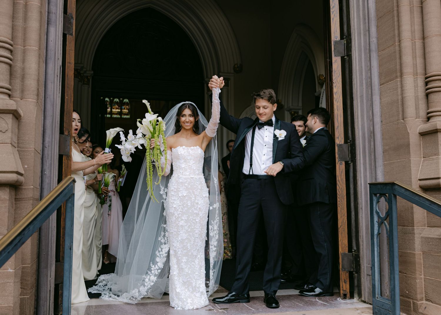 Wedding ceremony attendees line up outside ornate stone church entrance.