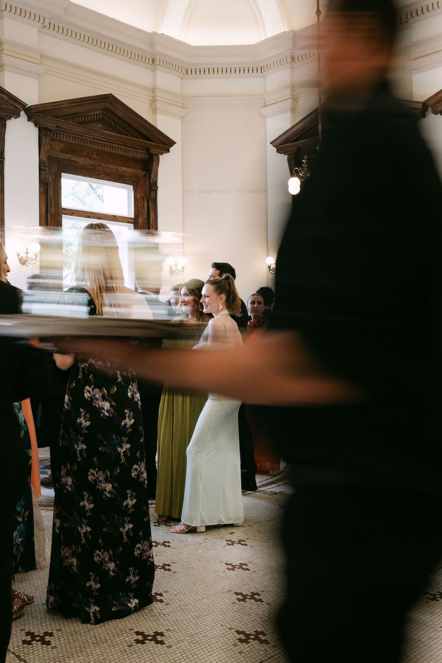 Elegant wedding reception interior with guests mingling, bride visible in white gown amid blurred motion.