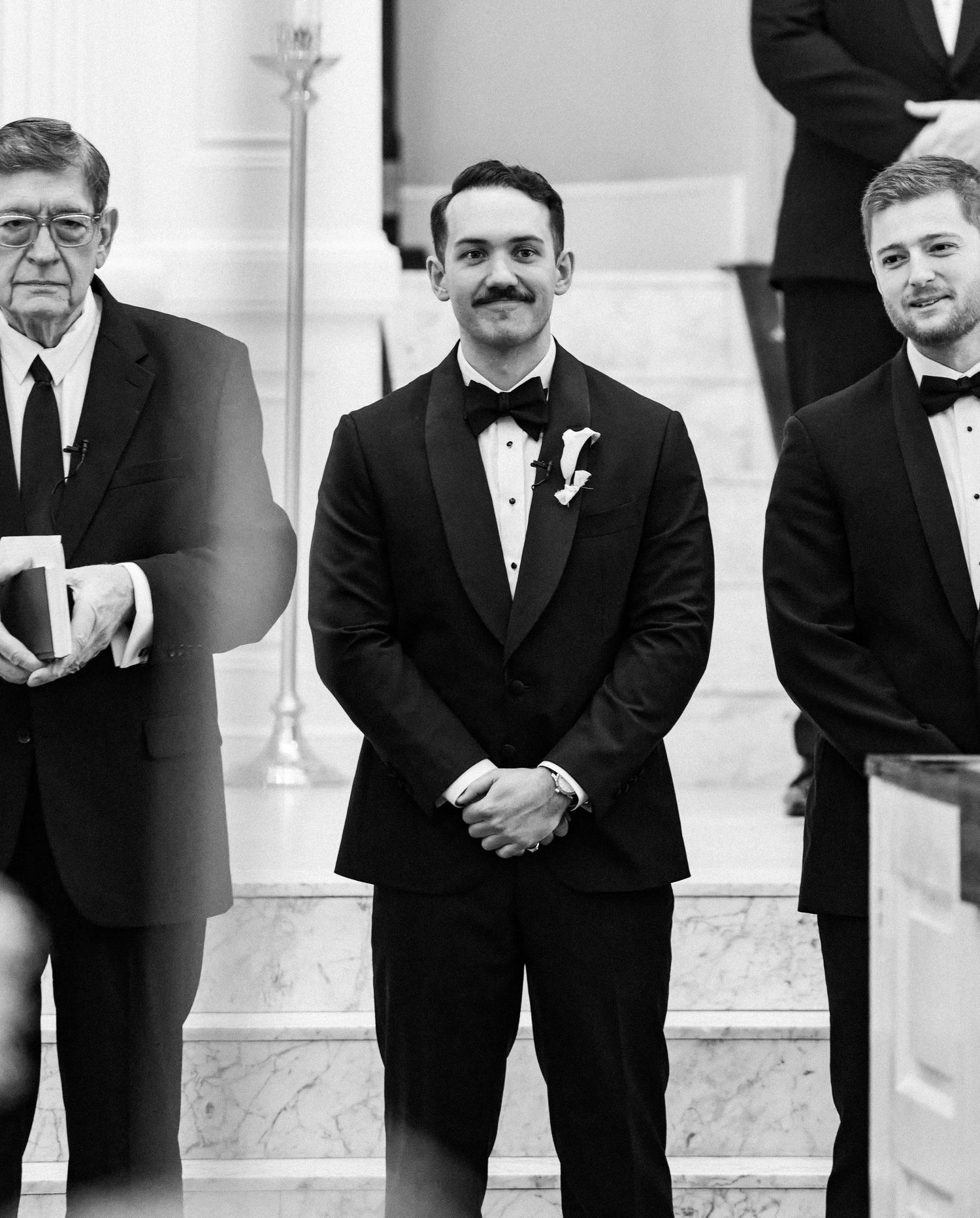 Black and white photo of three men in tuxedos standing at a wedding ceremony altar.