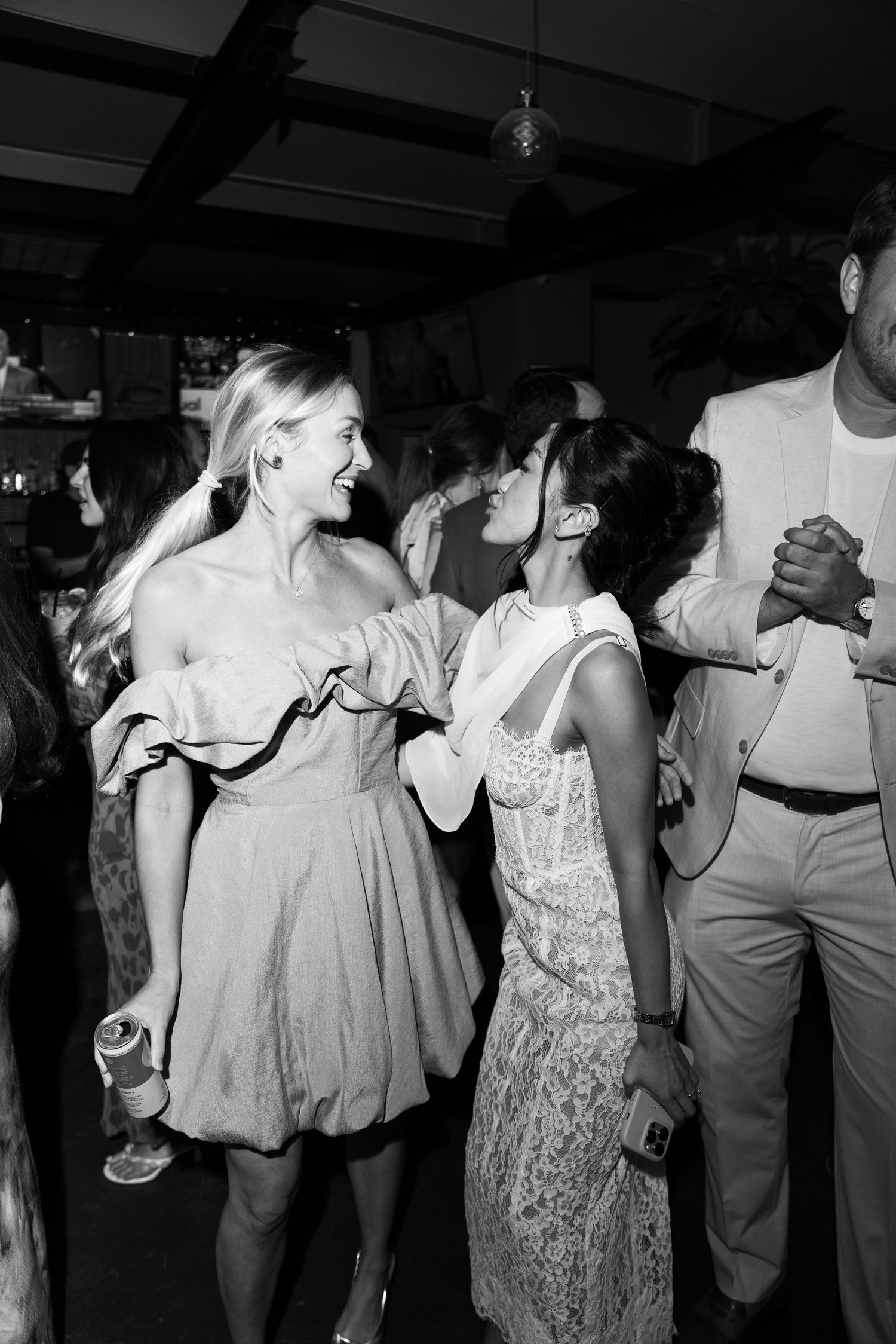 Two women dancing and laughing together at a lively party in black and white photo.