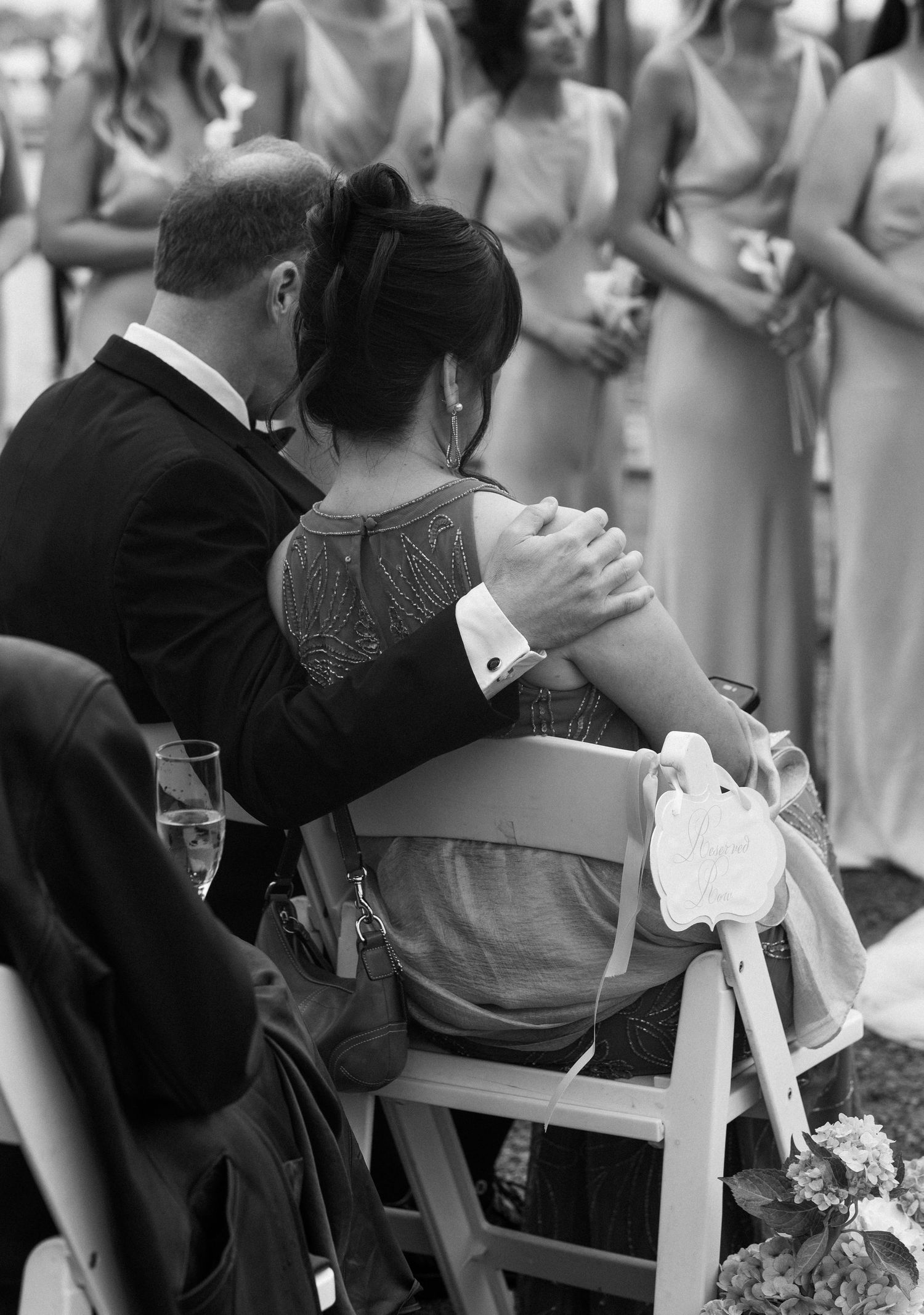 Couple embracing at outdoor wedding ceremony in black and white photo with bridesmaids behind.