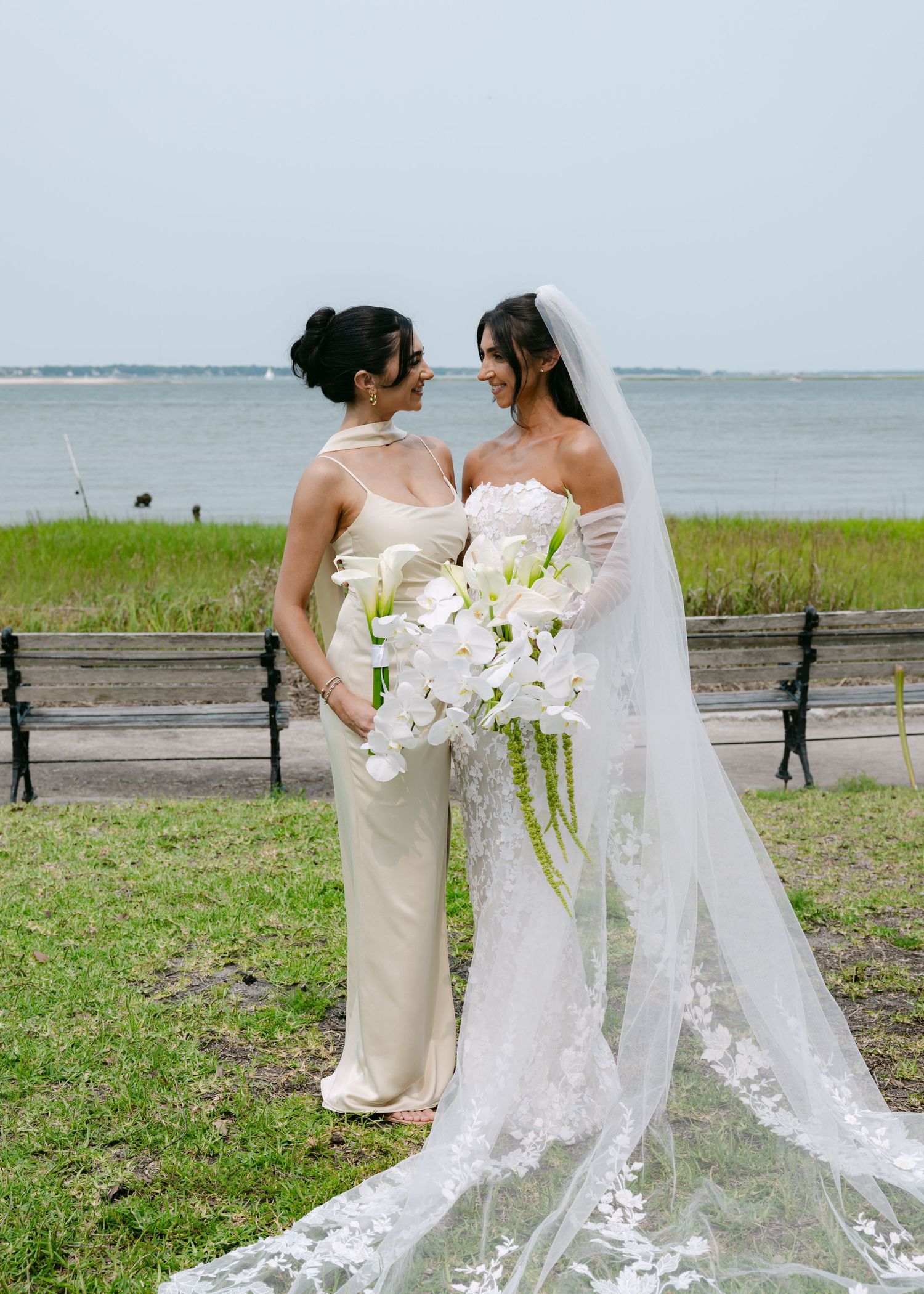 Elegant wedding party photos taken on grassy coastline with lace dress details.