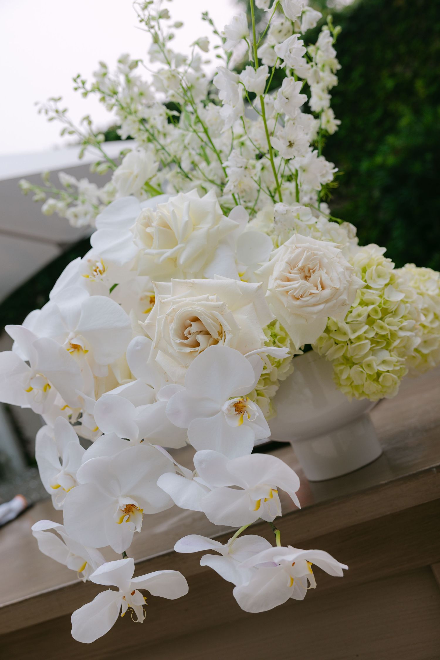 Elegant white orchids and roses arranged on a wooden surface against a dark background.
