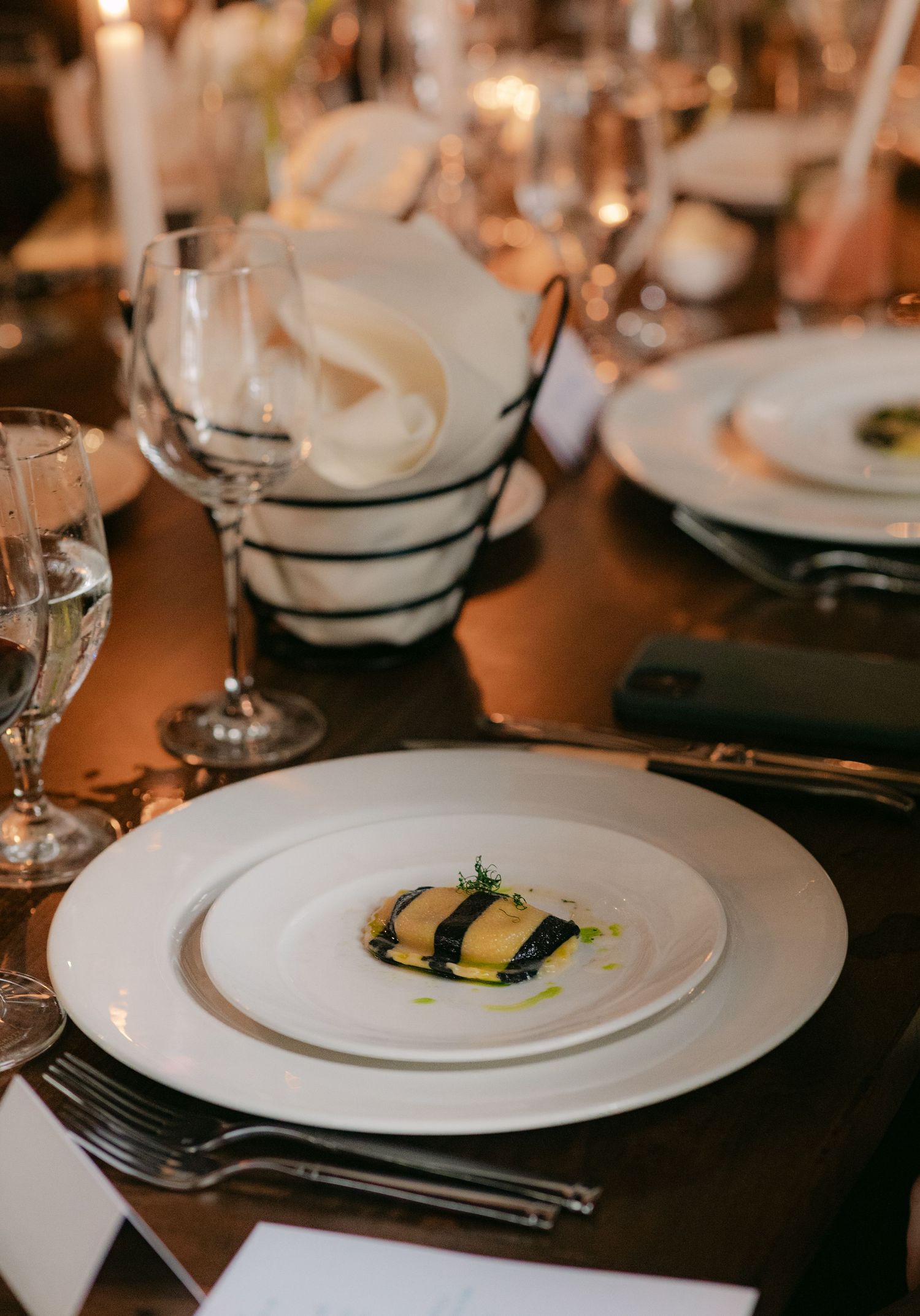 Elegant place settings with white plates and wine glasses at wedding reception.
