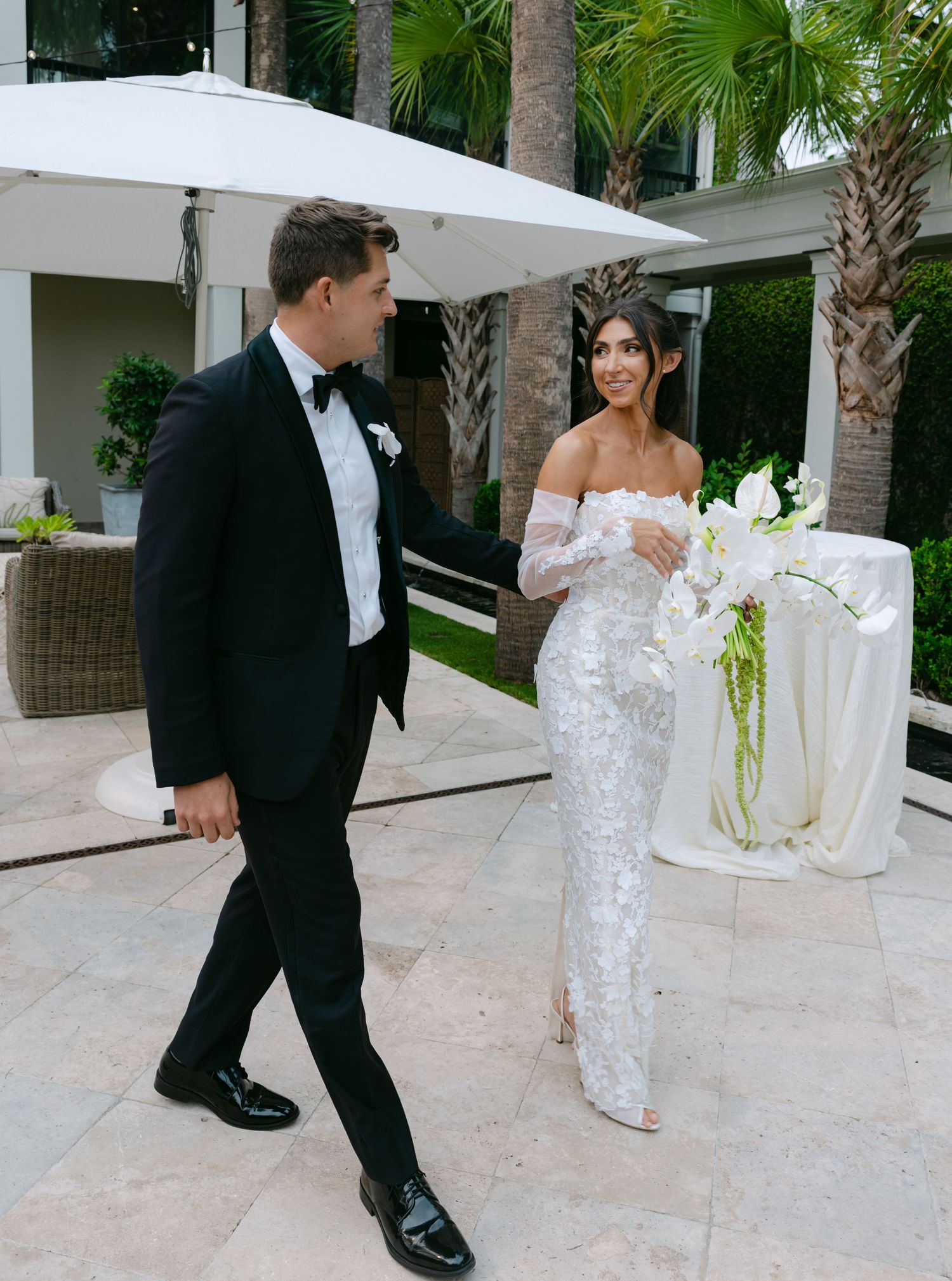 Wedding couple walks through elegant palm-lined courtyard with stone pavers.