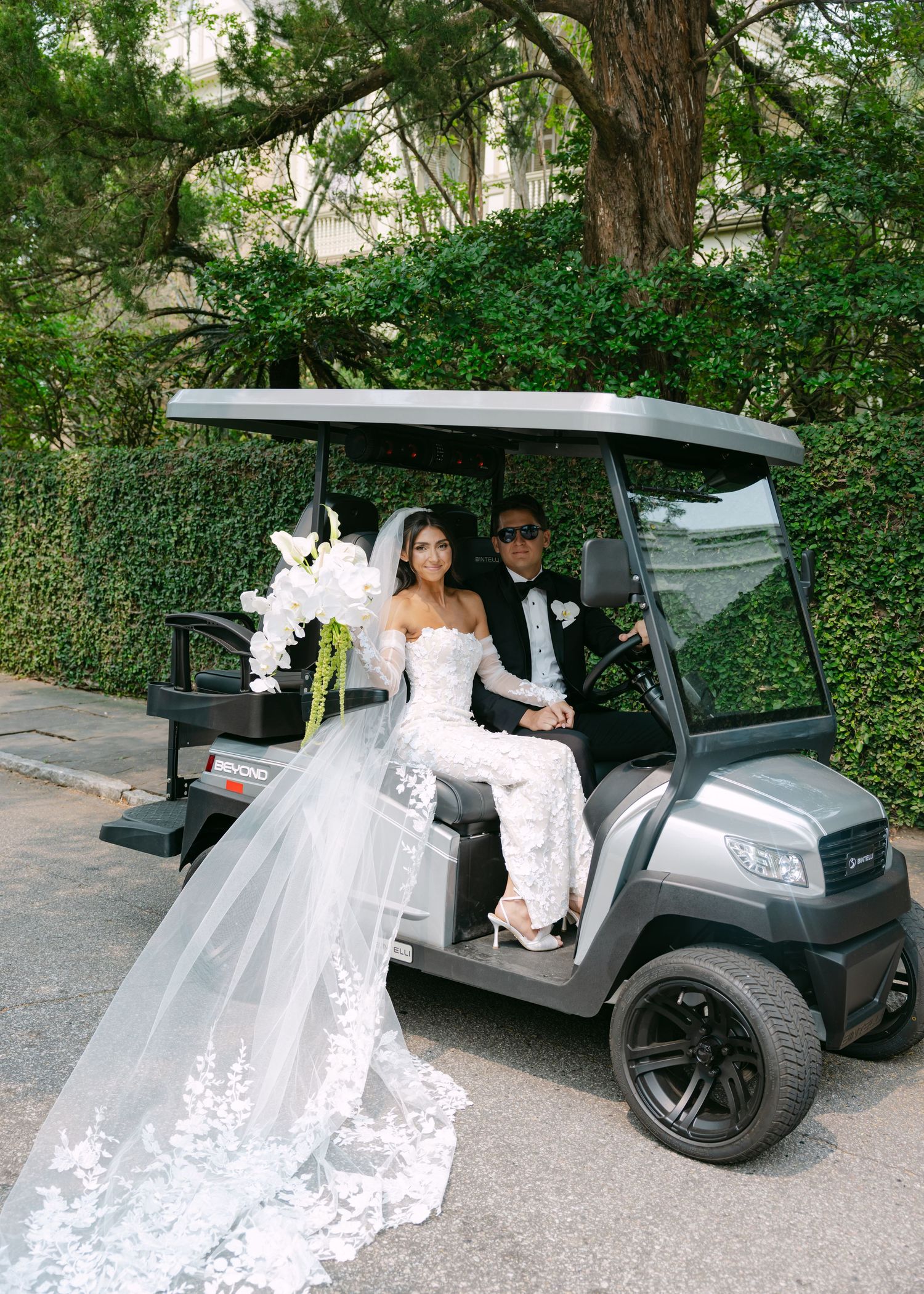 Bride in a stunning lace gown poses with golf cart transportation at an elegant outdoor venue.