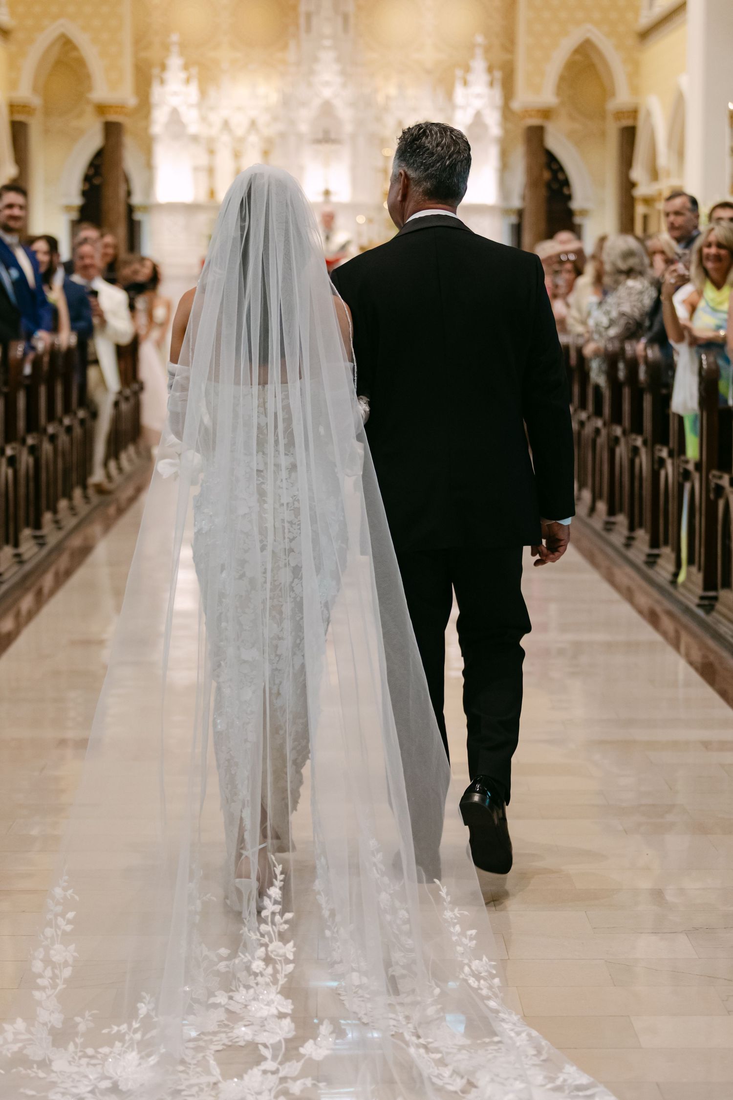 Long cathedral veil with lace details trails behind during church wedding ceremony.