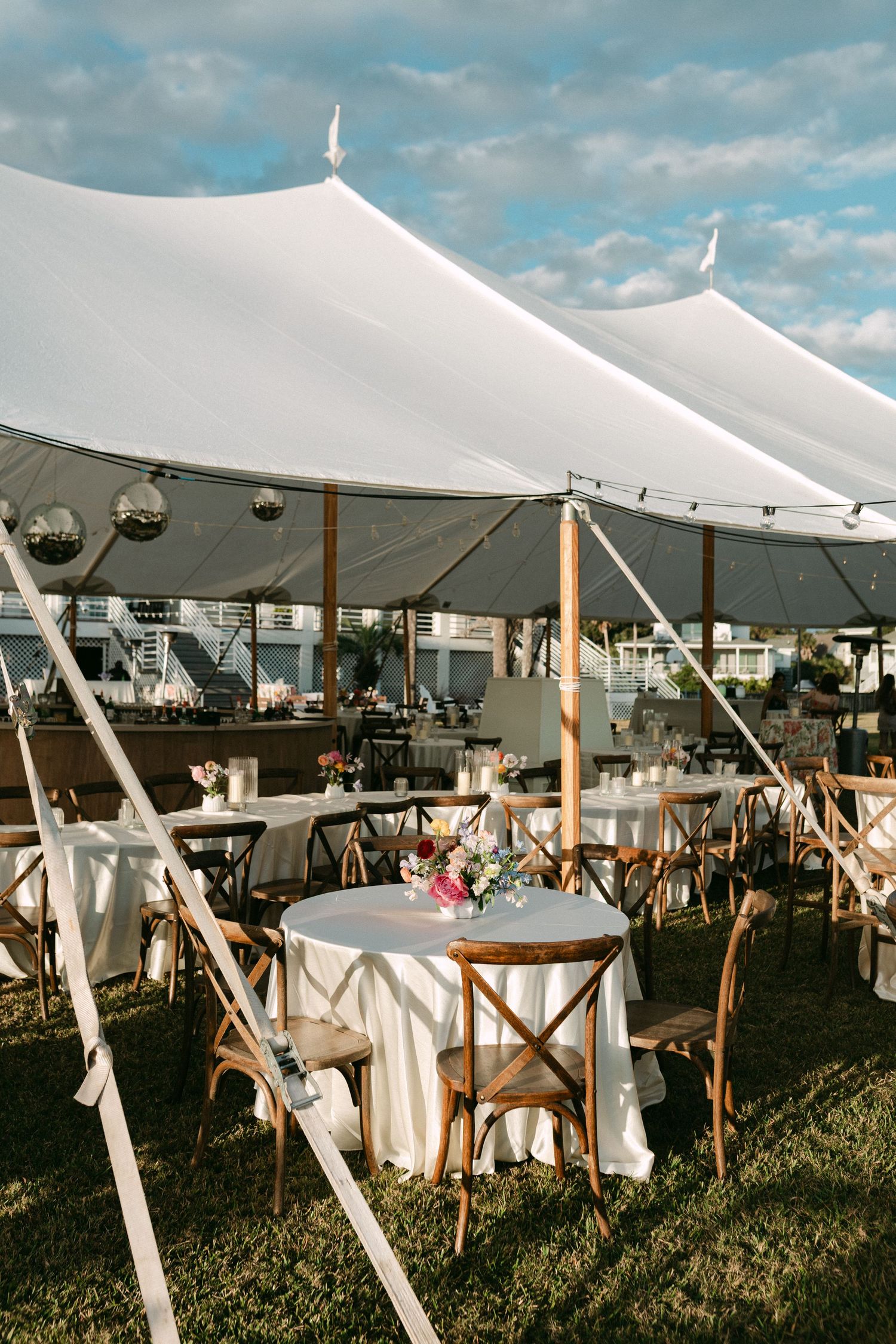 Elegant outdoor wedding reception under white sailcloth tent with wooden chairs and floral centerpieces.