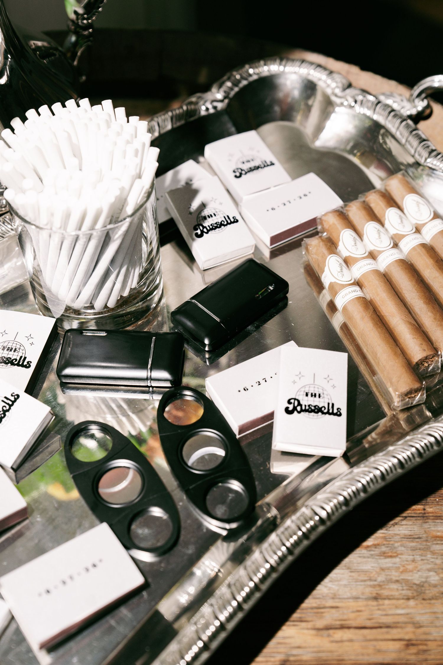 Silver tray displaying cigars, branded matchbooks, cigar cutter, and accessories for wedding cigar bar.