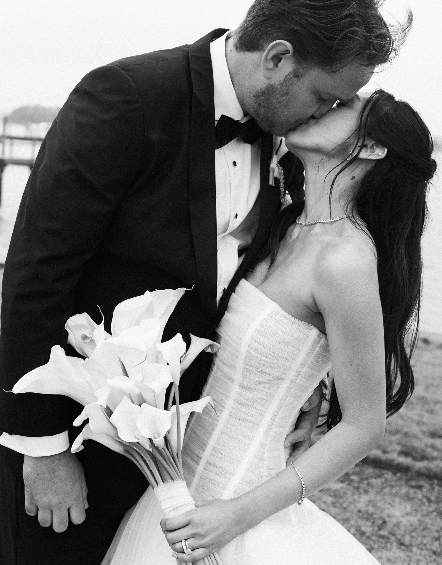 Black and white photo of a bride and groom sharing a kiss, bride holding calla lily bouquet in strapless gown.