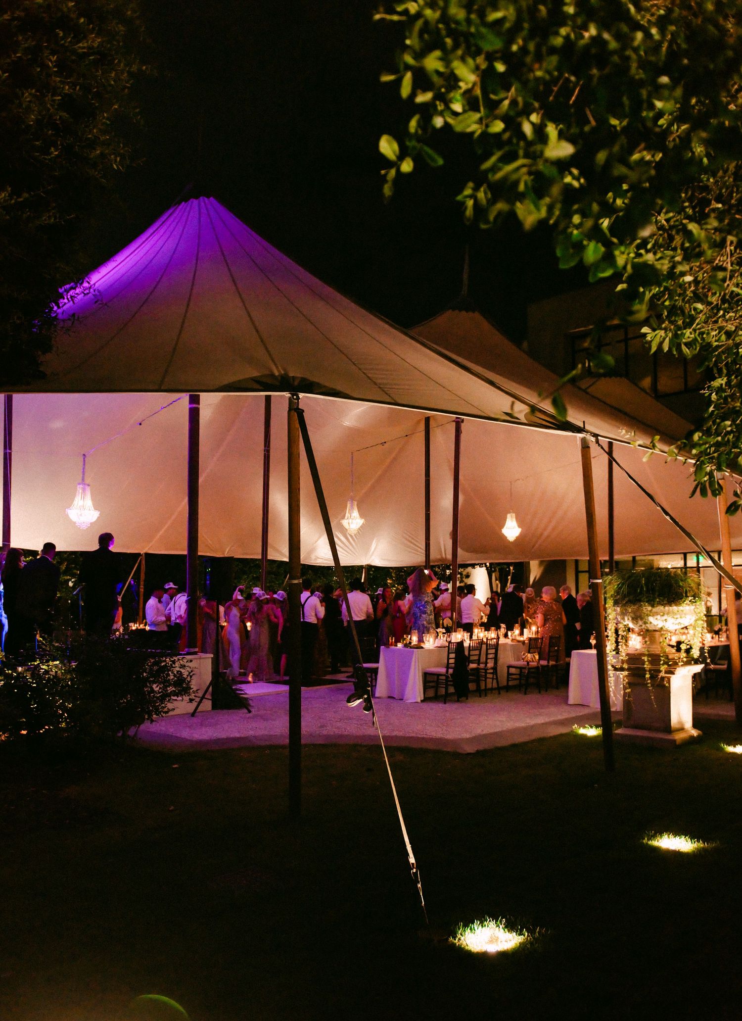 Outdoor wedding reception under a tent with warm lighting and purple accents at night.