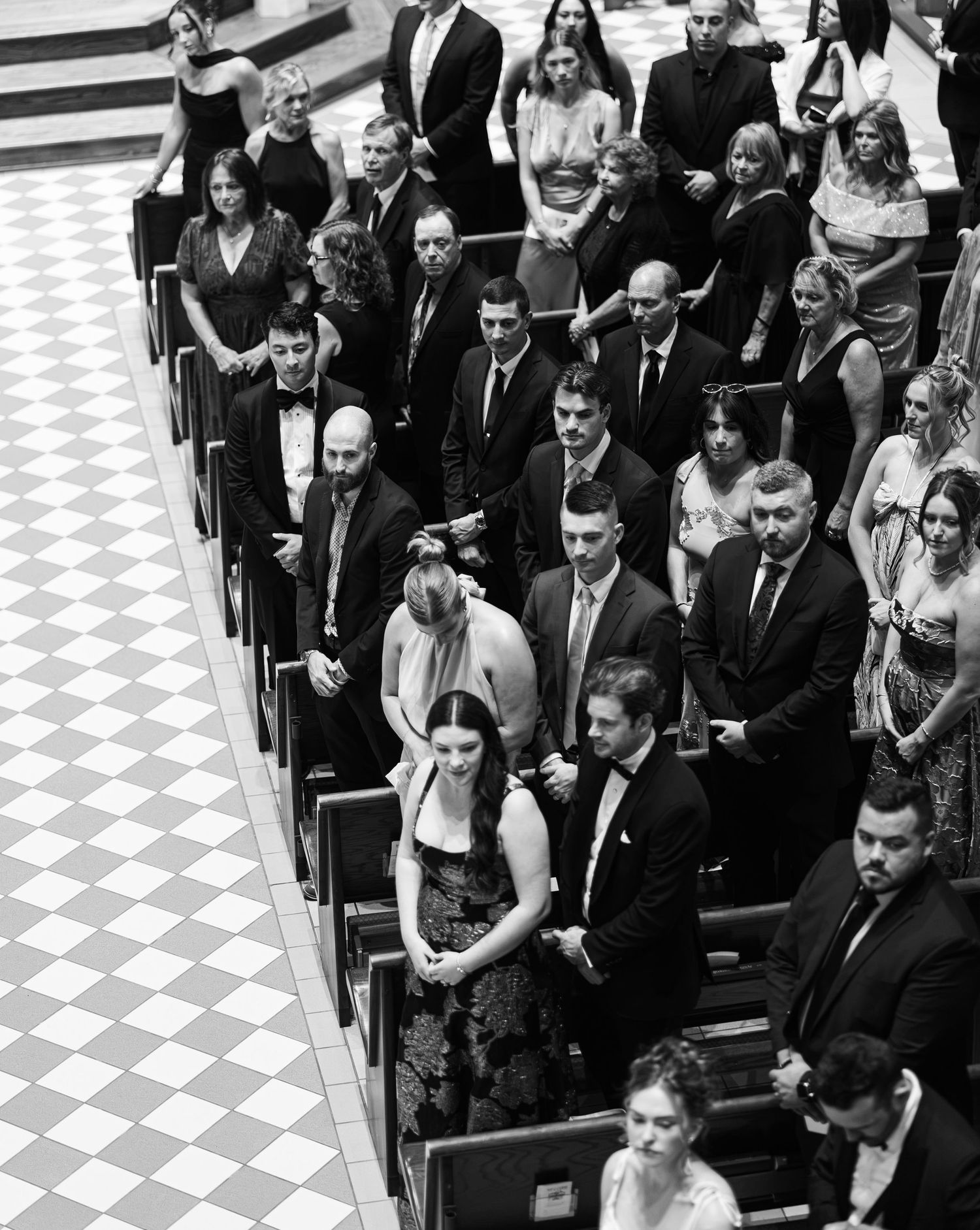 Black and white aerial view of wedding guests standing in church pews during a formal ceremony.
