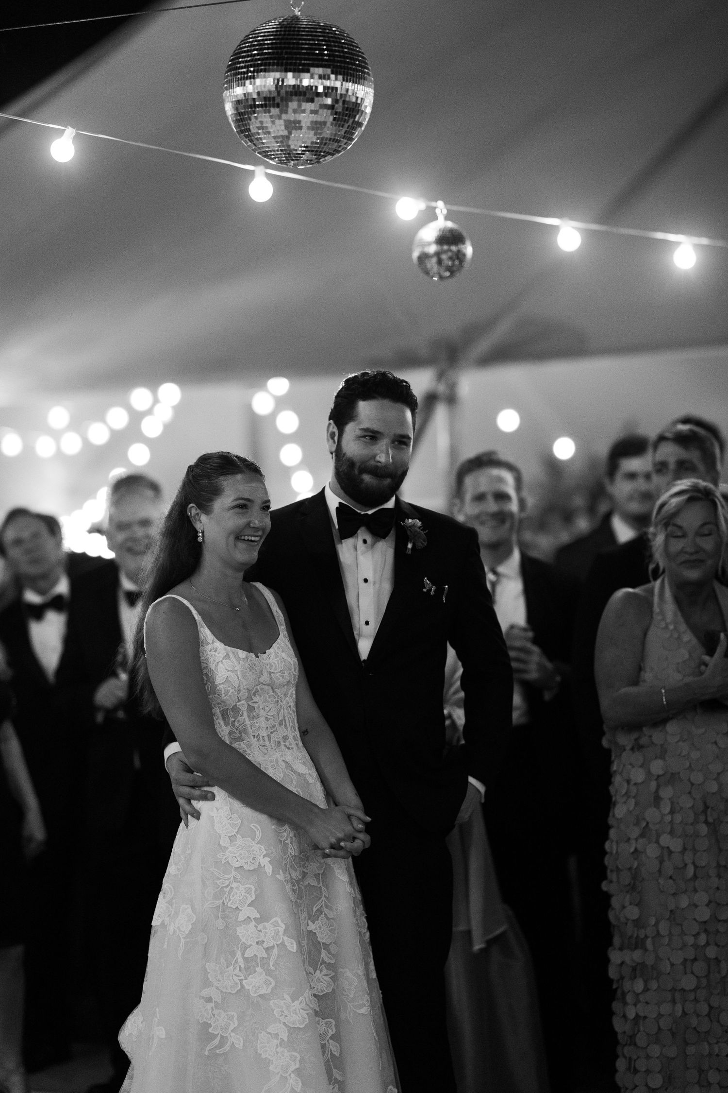 Black and white photo of bride and groom sharing first dance under disco ball in tent.