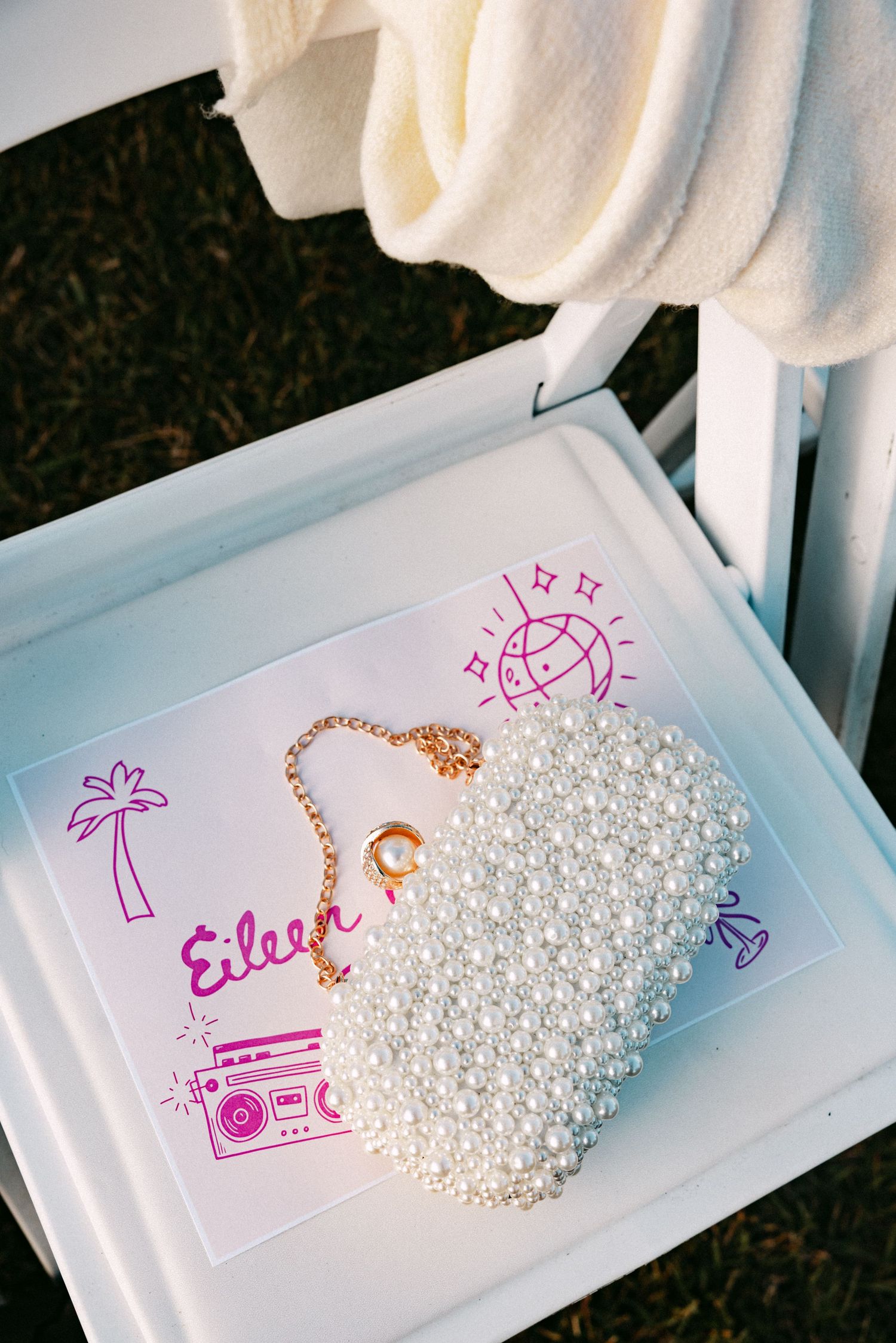Pearl heart-shaped bridal clutch rests on a personalized wedding place card on a chair.