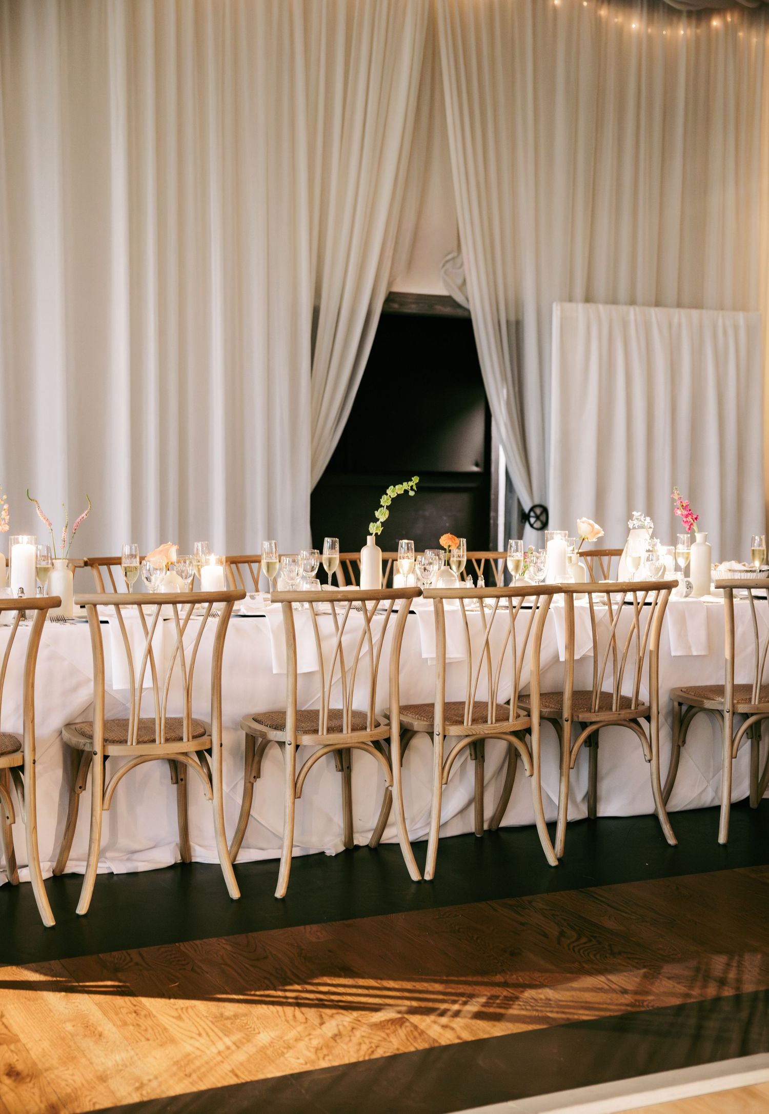 Elegant wedding reception with long white draped tables, gold crossback chairs, and candles.