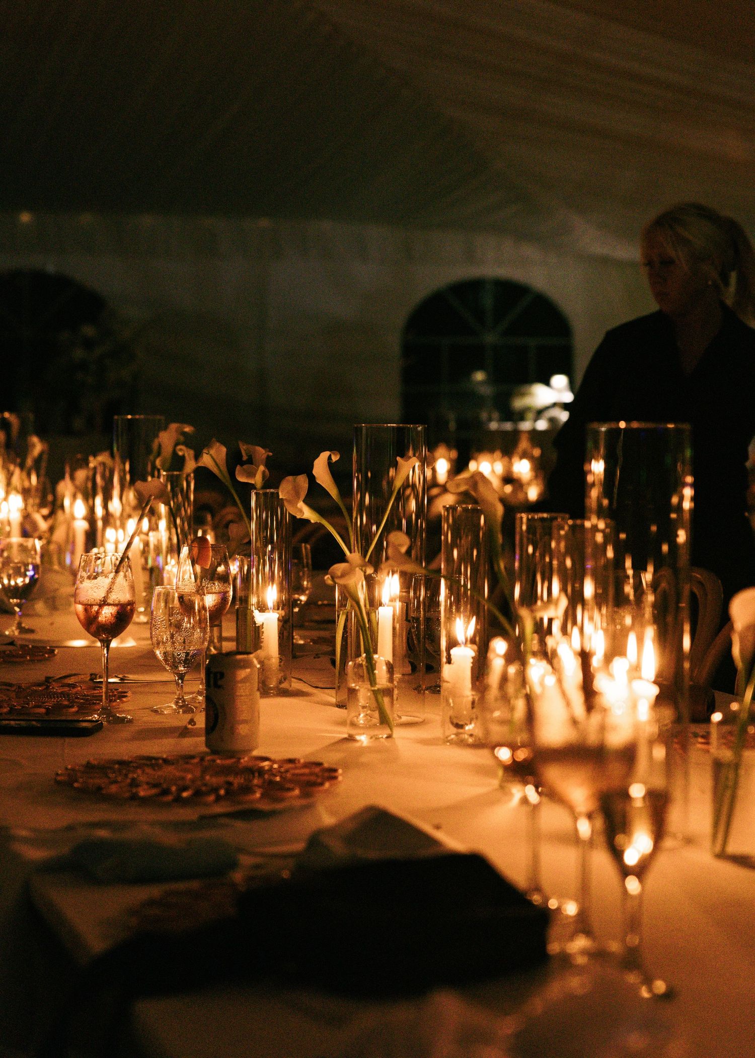 Elegant candlelit dinner table with tall glass vases, white calla lilies, and glowing candles creating a romantic ambiance.