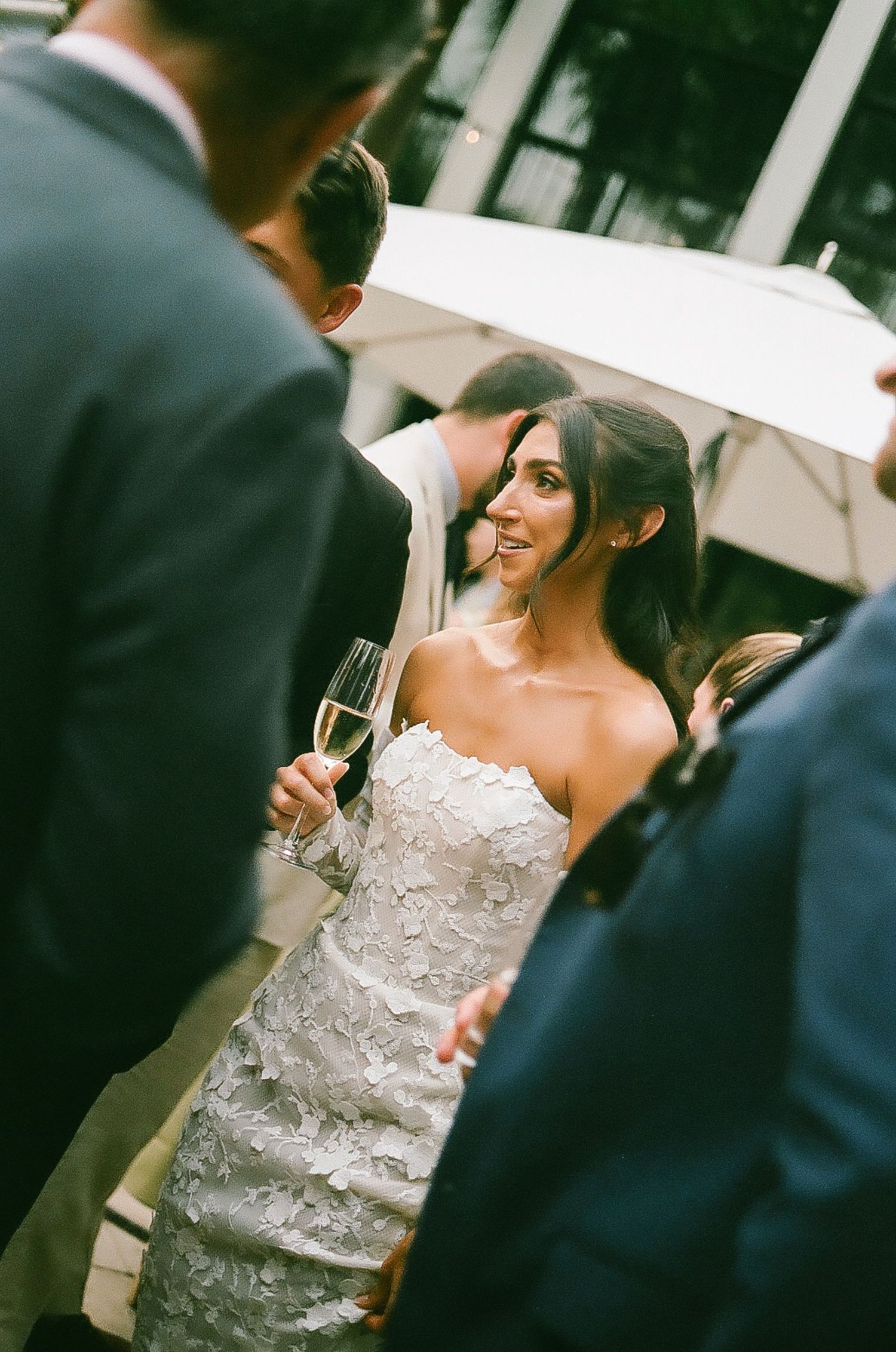 A candid moment during a wedding reception shows guests mingling with drinks in hand.