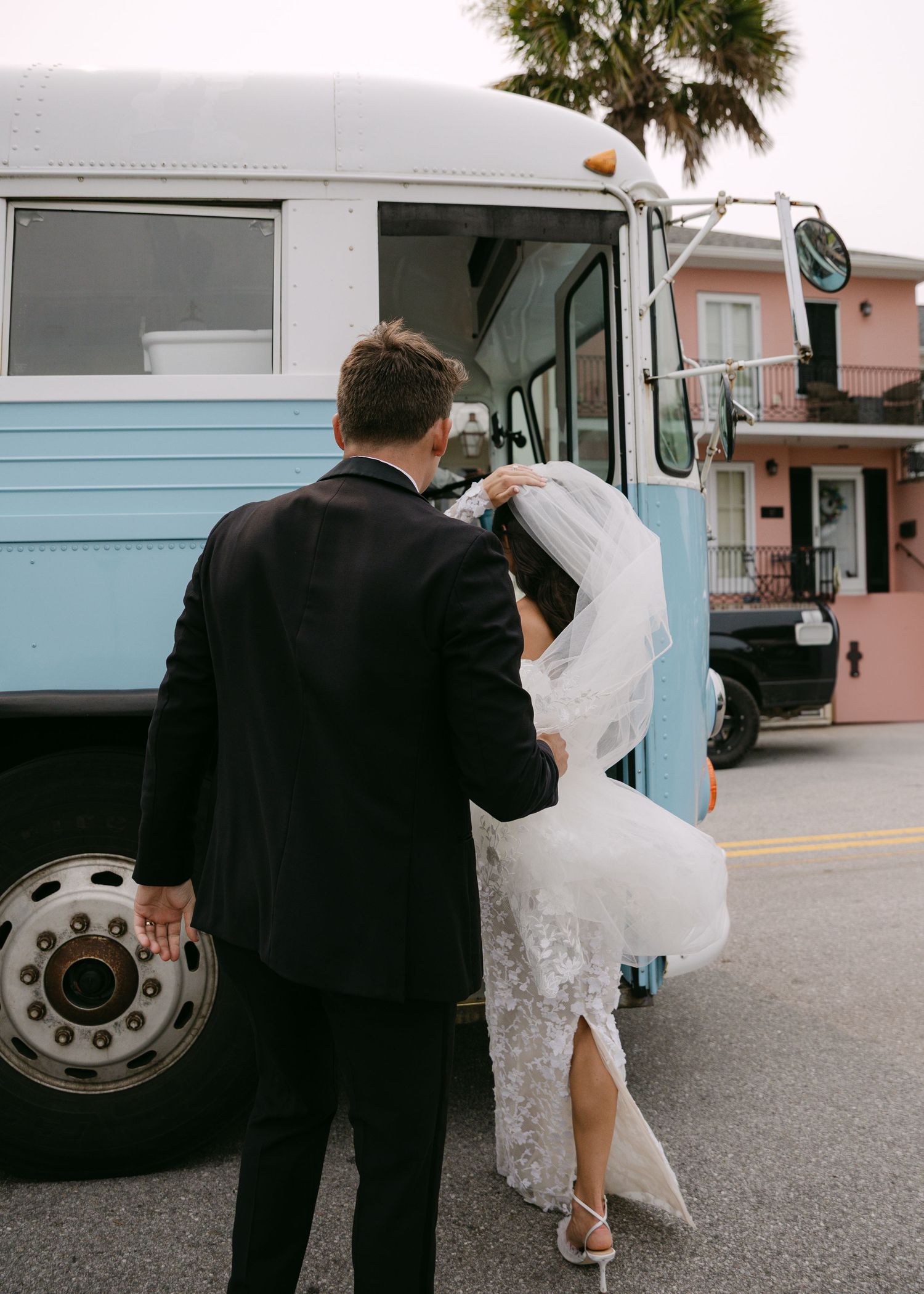 Wedding couple poses next to vintage blue and white bus during outdoor photo session.