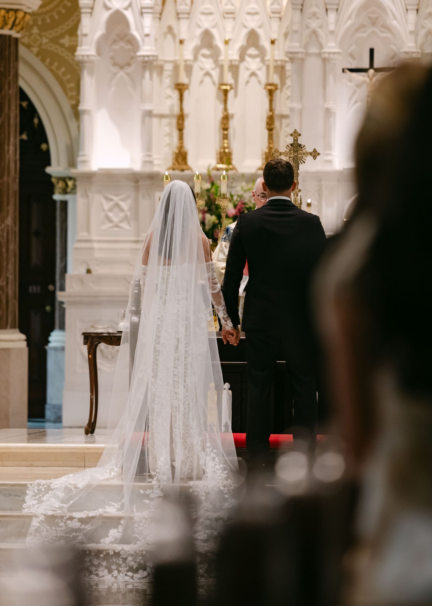 A couple stands at the altar of an ornate Catholic church during their wedding ceremony.