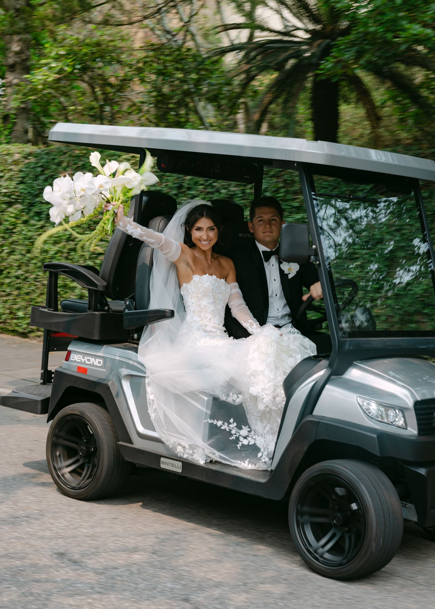 Stylish black golf cart carries newlyweds through a lush garden setting.