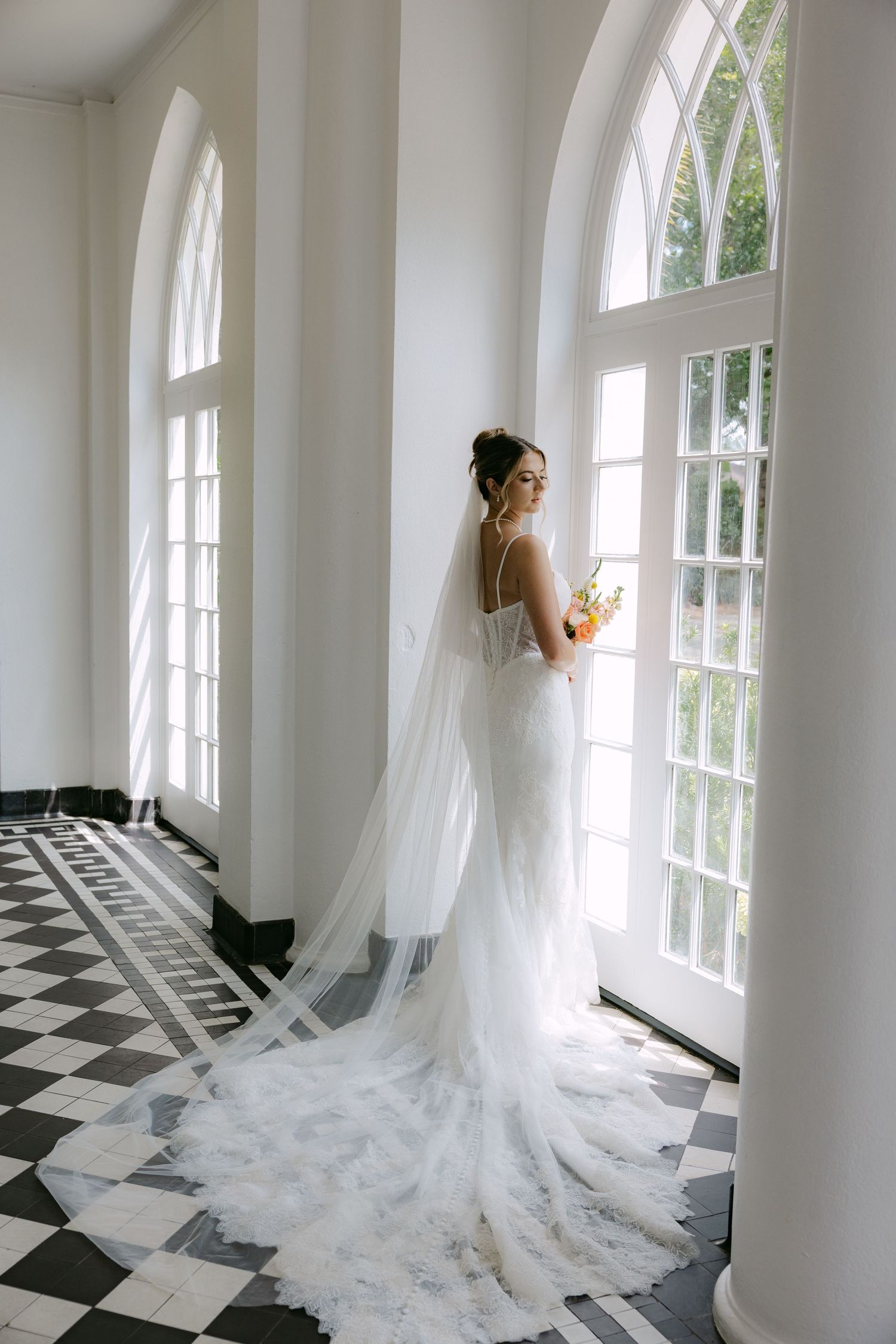Dramatic bridal portrait in white gown with flowing train against black and white checkered floor.