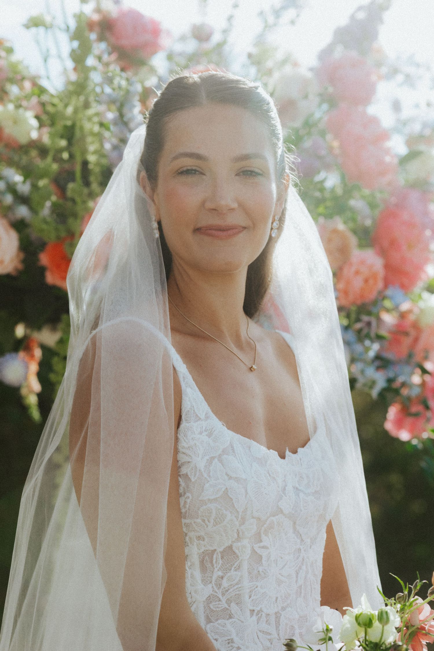 Close-up portrait of a bride wearing a delicate lace wedding dress and flowing veil in a garden setting.