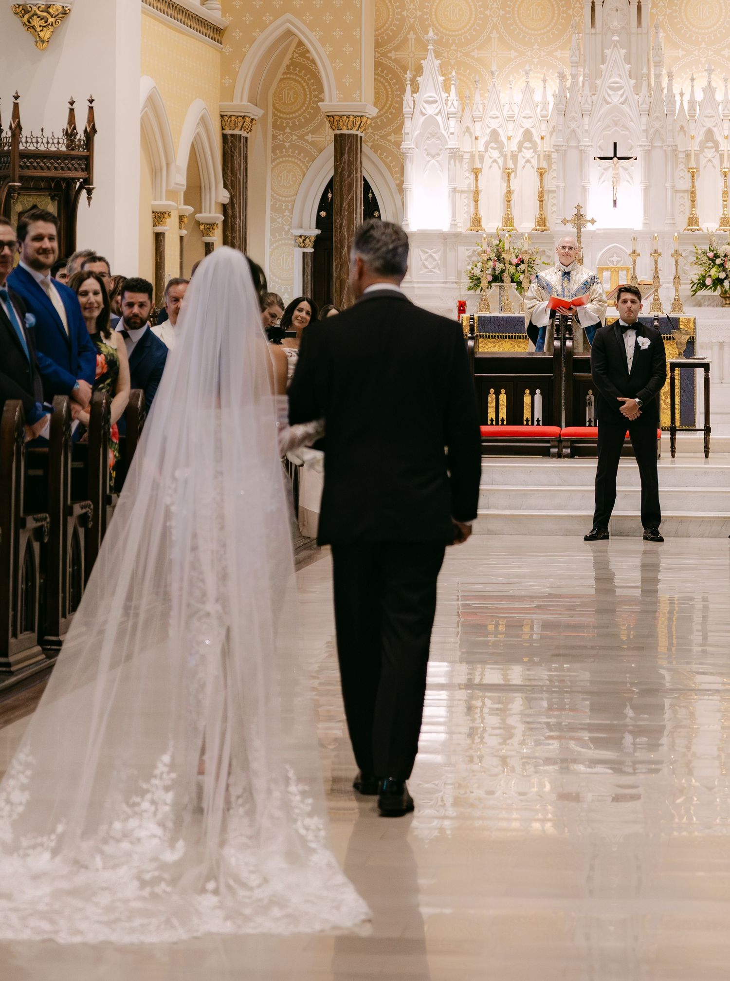 Wedding processional in a bright cathedral with flowing veil trailing behind.