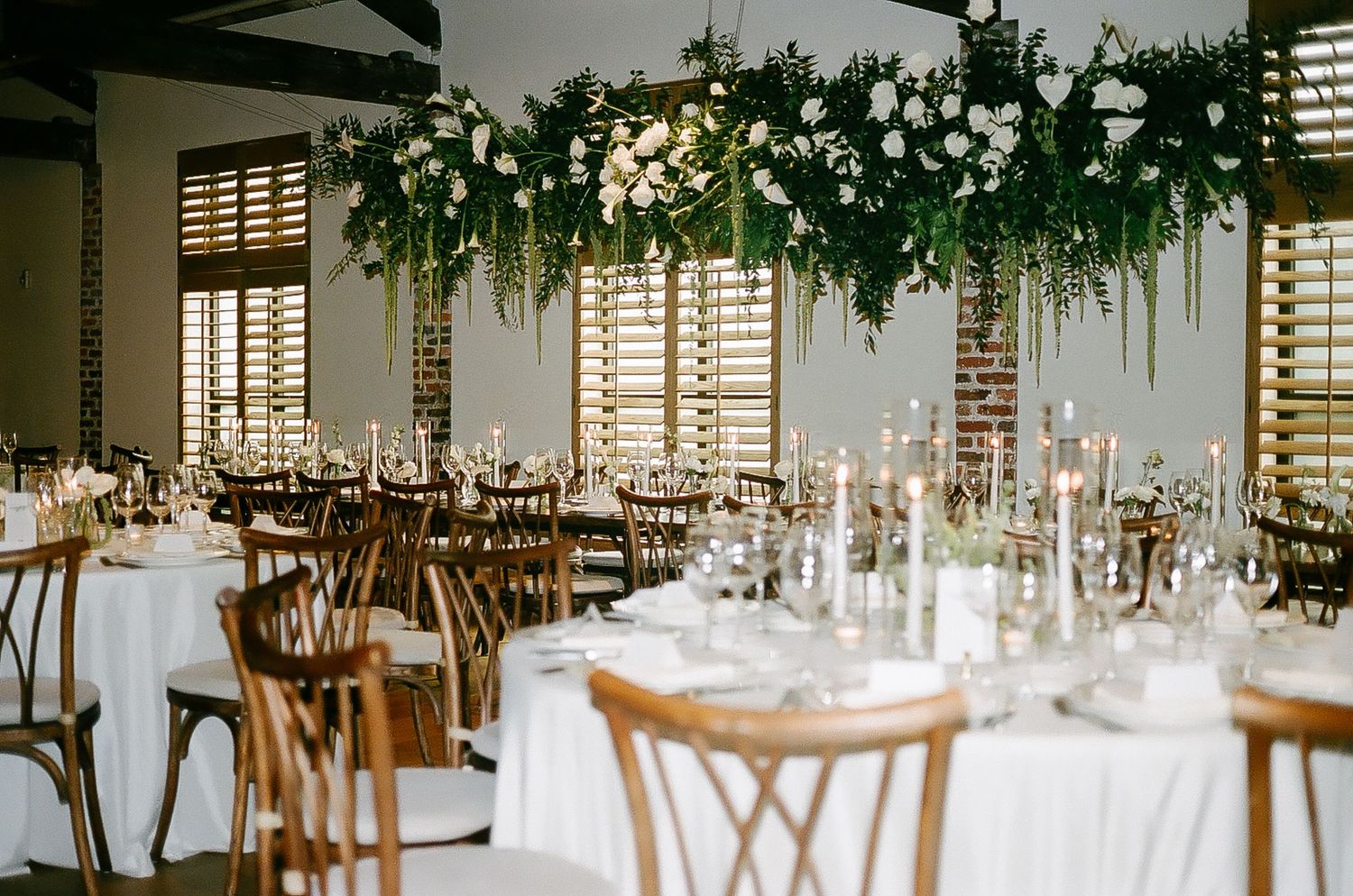 Elegant wedding reception tables decorated with greenery and hanging lights.