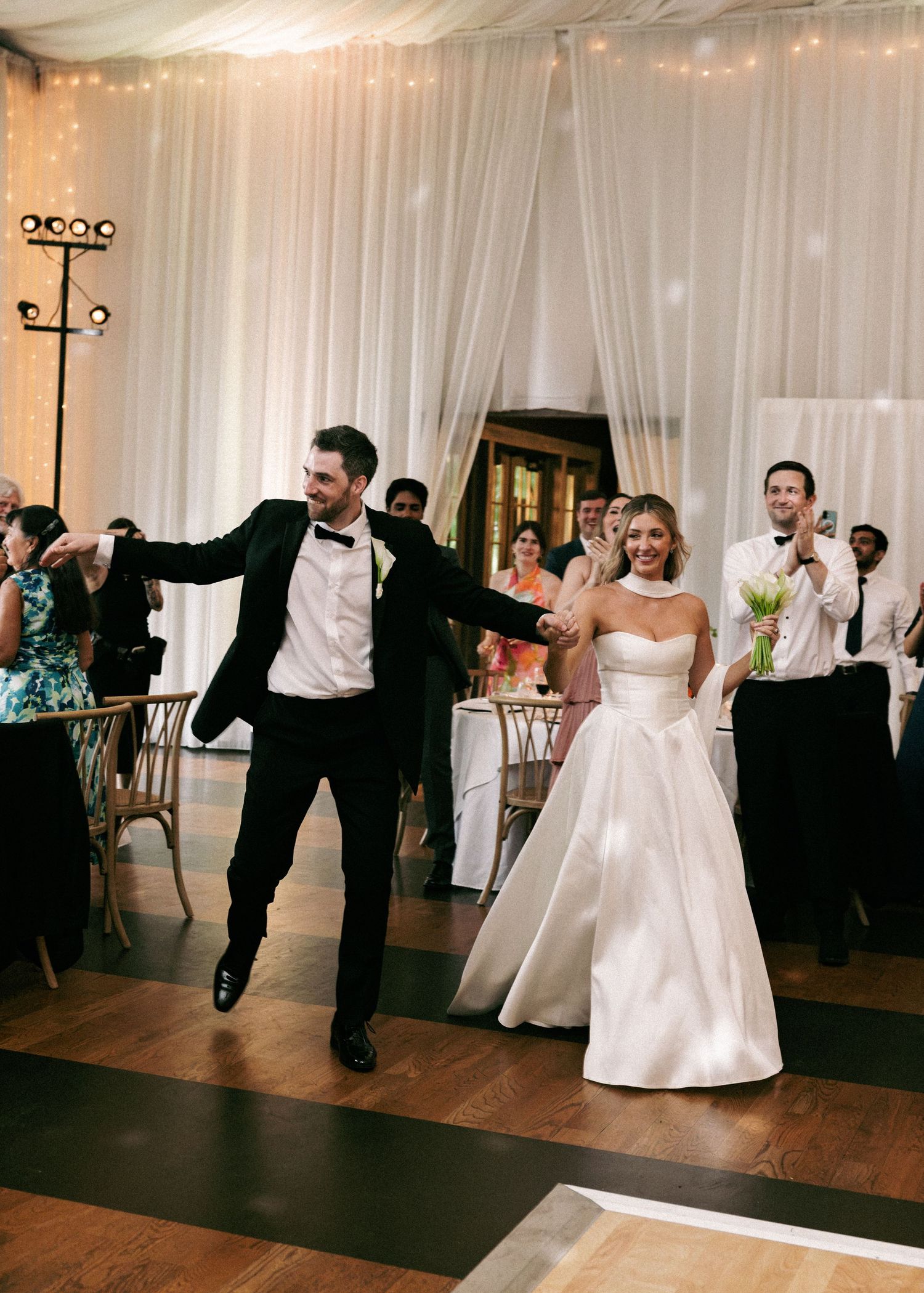 Joyful bride and groom make grand entrance onto dance floor at elegant tented wedding reception.