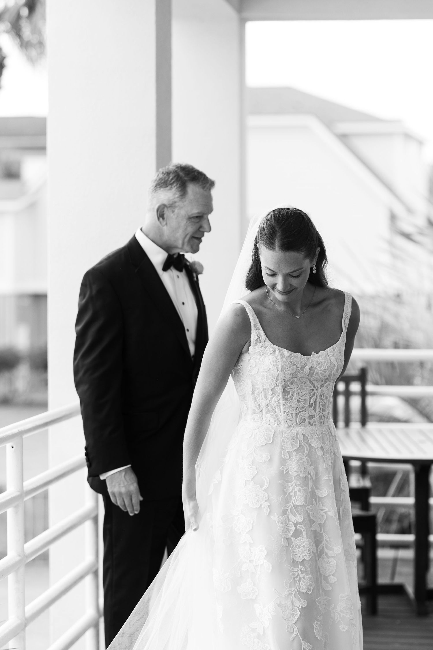 Black and white photo of bride in lace gown with father before outdoor beach wedding ceremony.