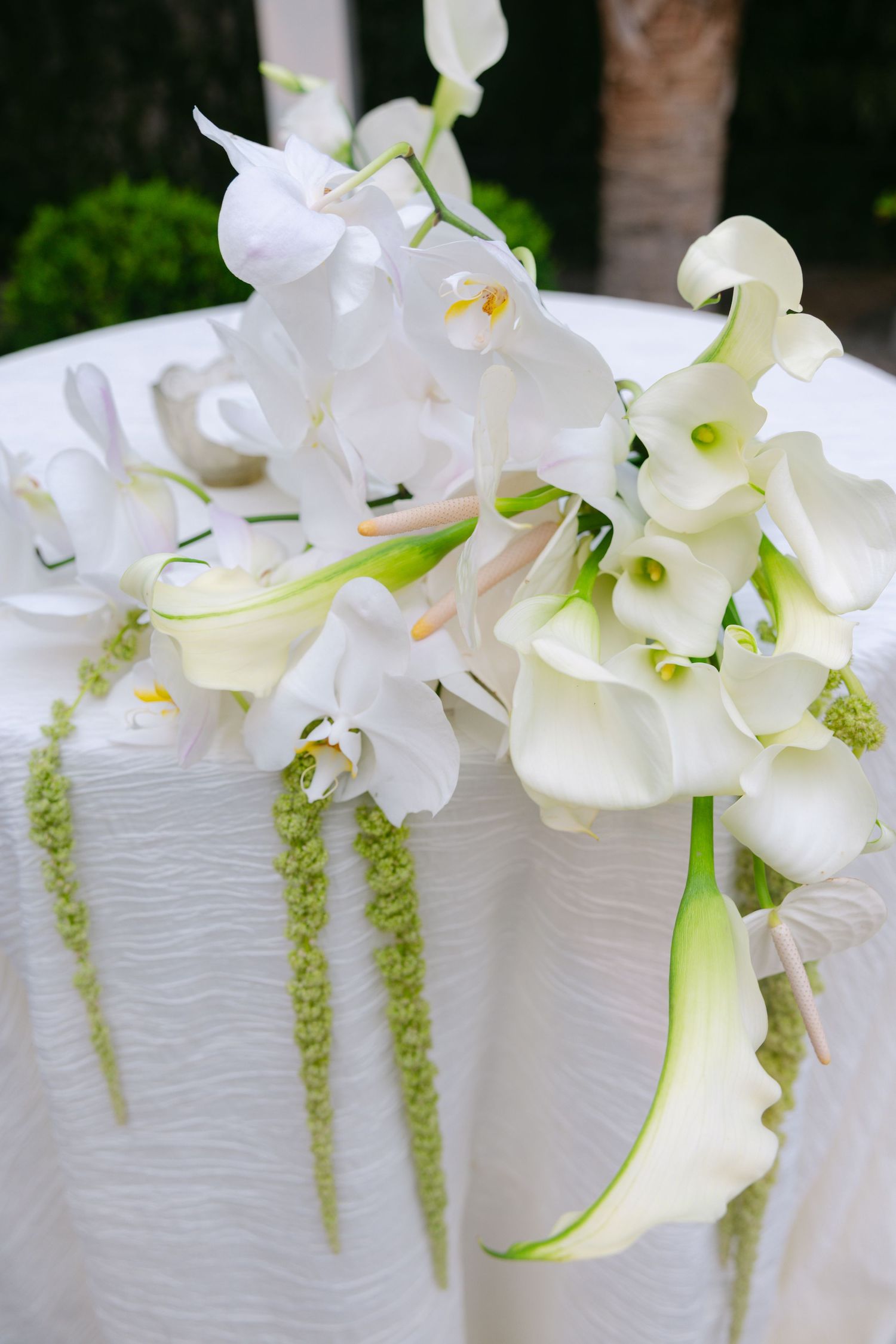 White orchids and calla lilies cascade along a textured wedding cake with delicate greenery accents.