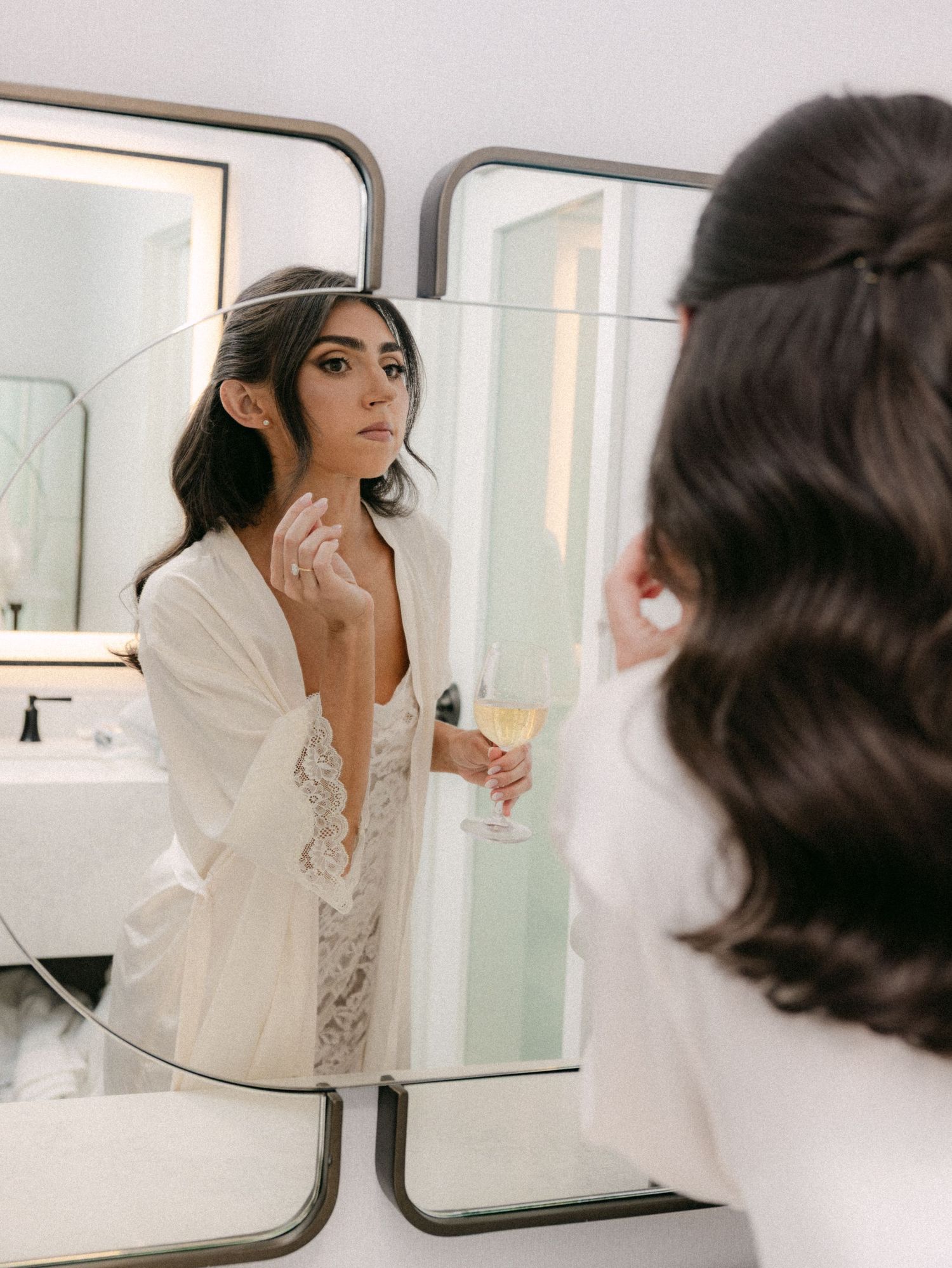 Figure in white robe applying makeup in bathroom mirror reflection.