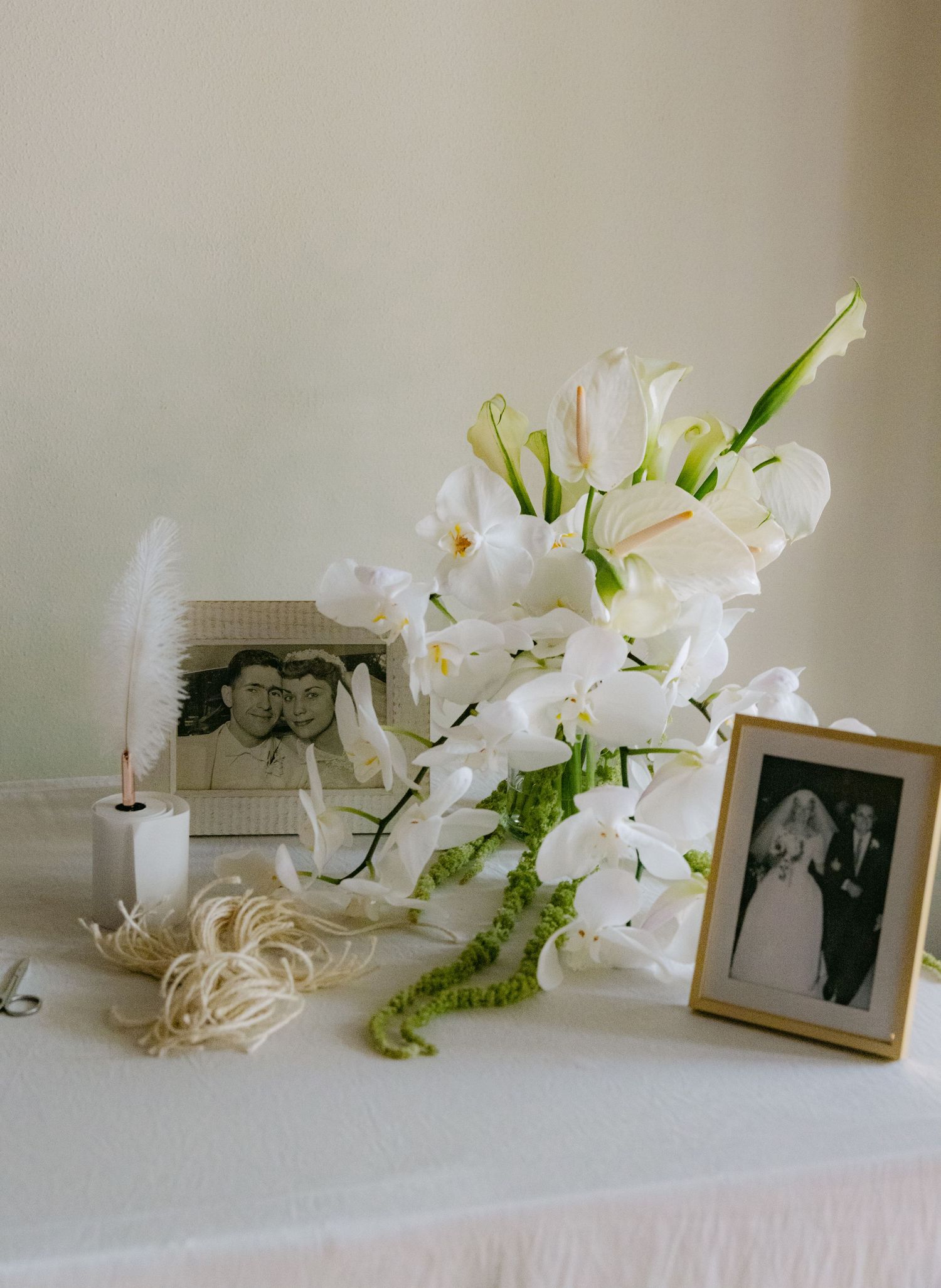 Wedding display with white orchids, vintage photographs and feather decorations.