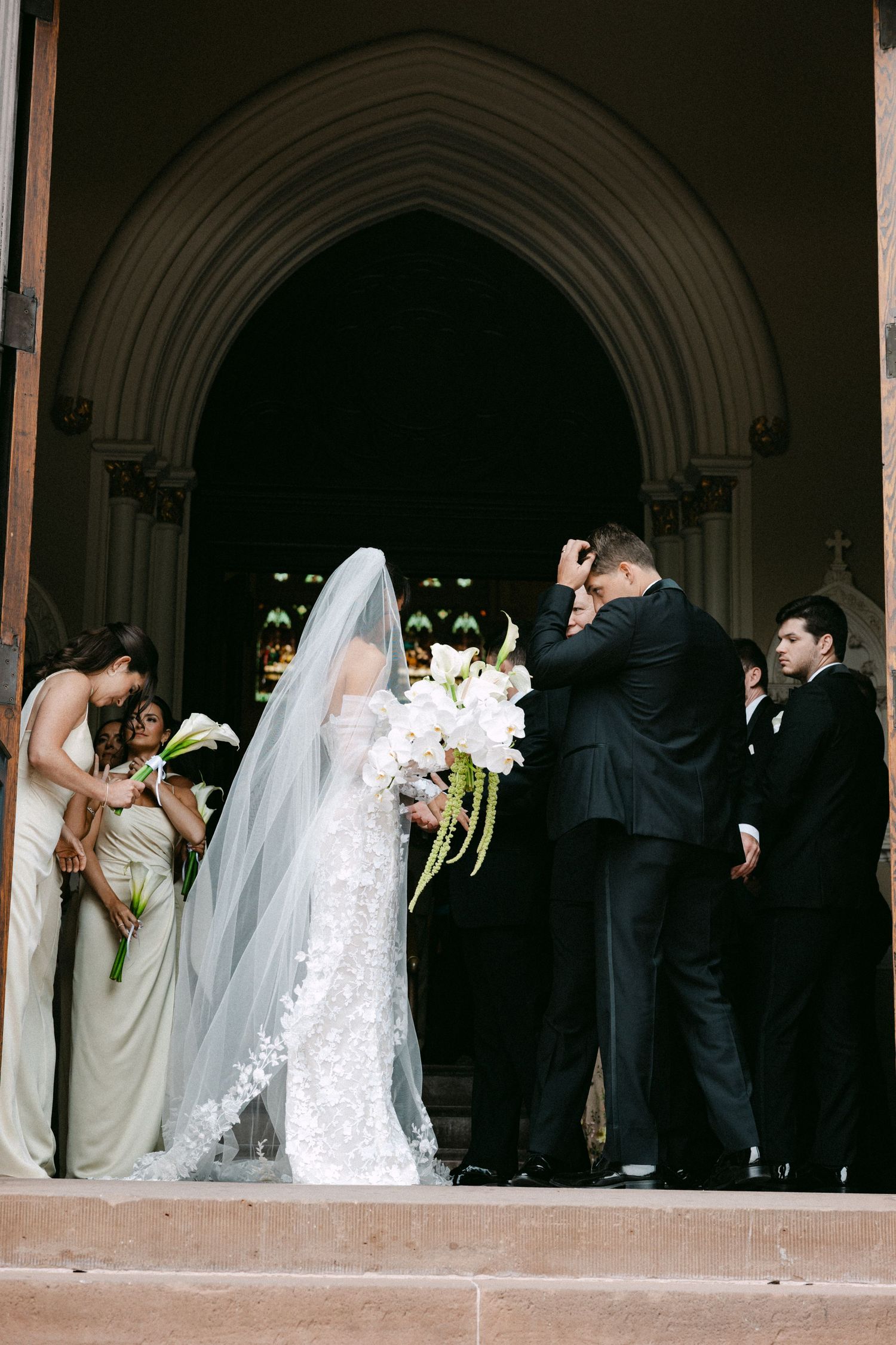 Wedding party gathered under arched church doorways during ceremony.