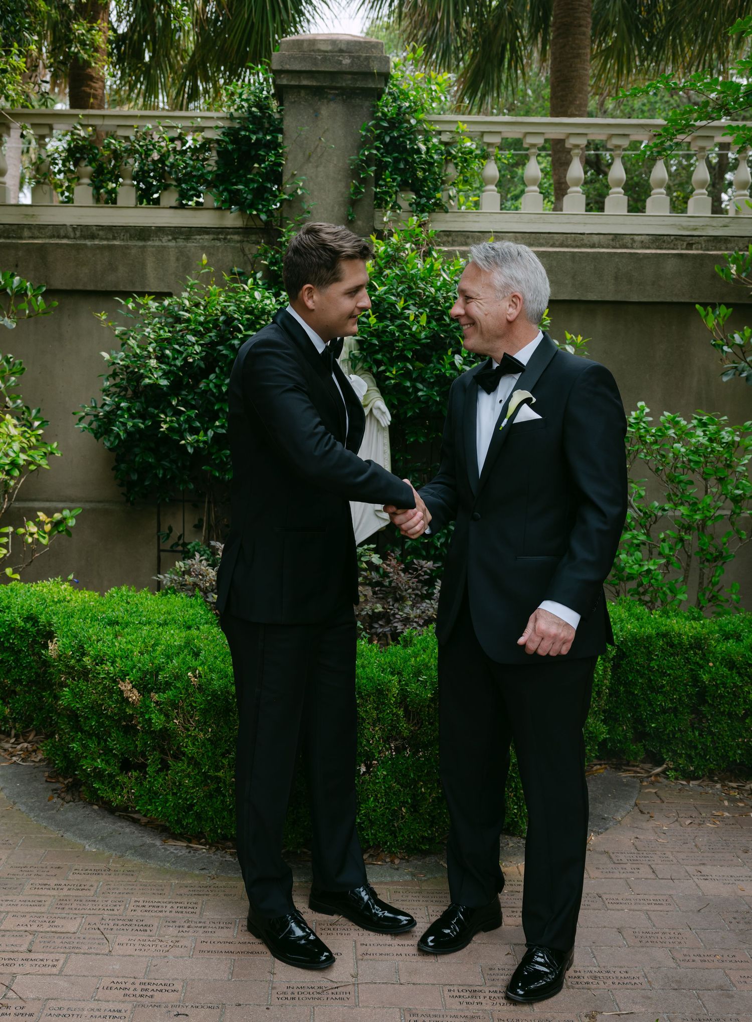 Formal wedding attire portrait showing black tuxedos against garden background.