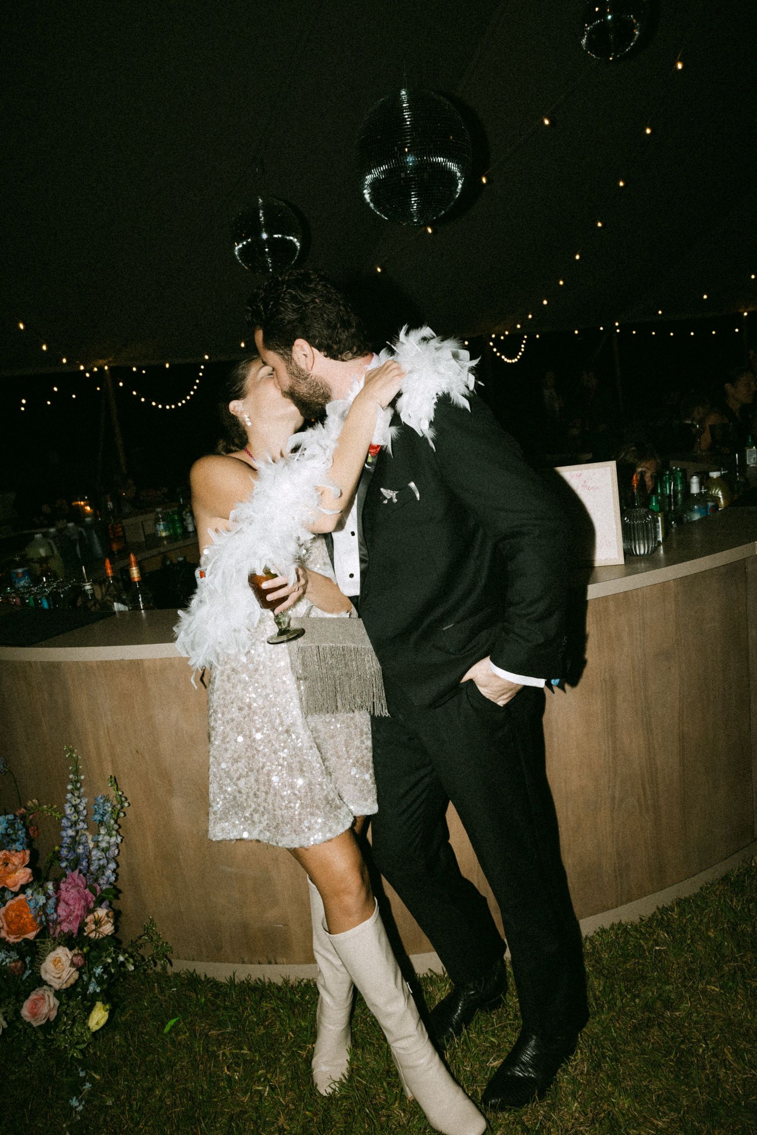 A couple in formal attire dances at night surrounded by sparklers and festive lights at an outdoor celebration.