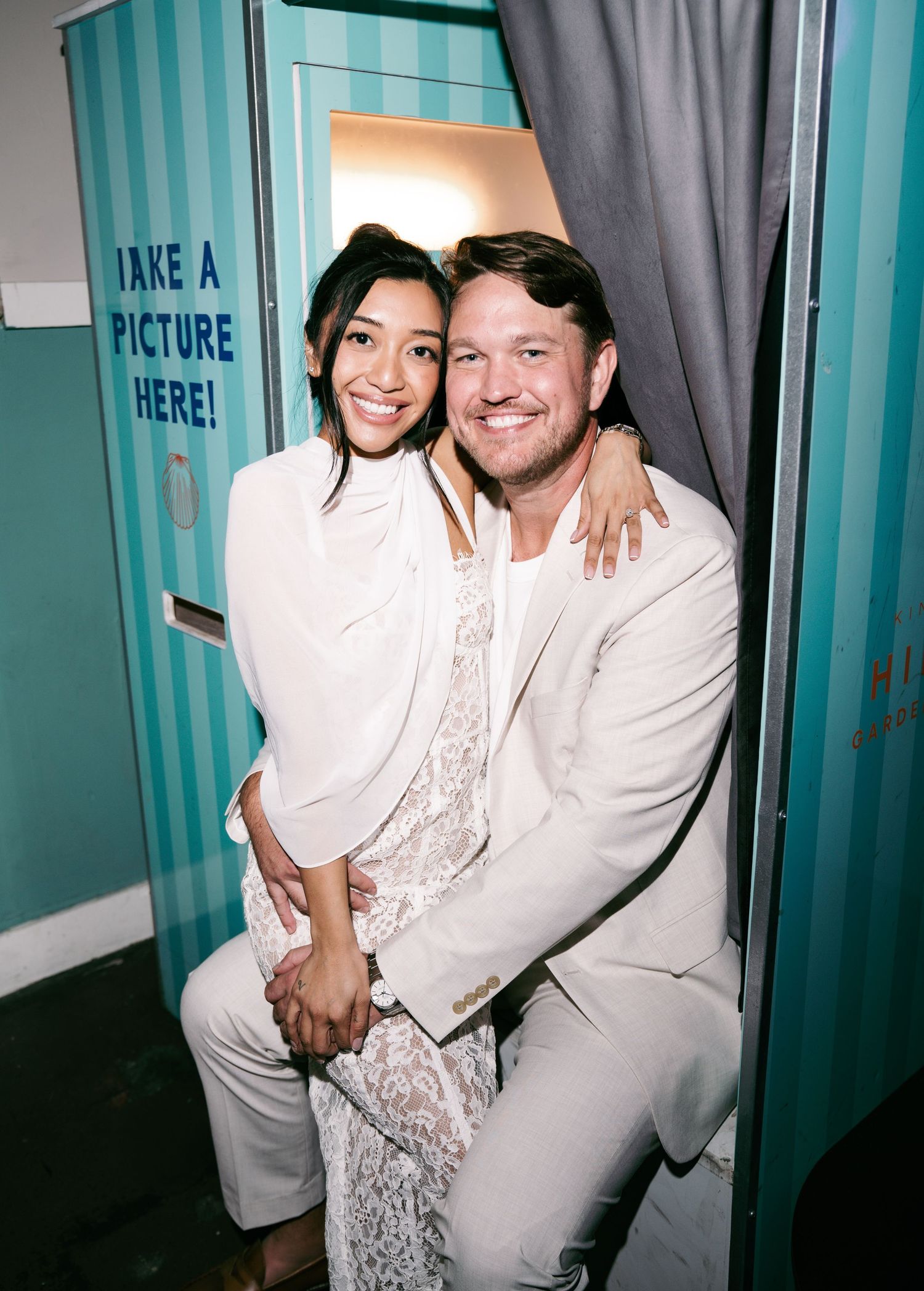 Couple smiling together in a photo booth with teal stripes and a Take a Picture Here sign.