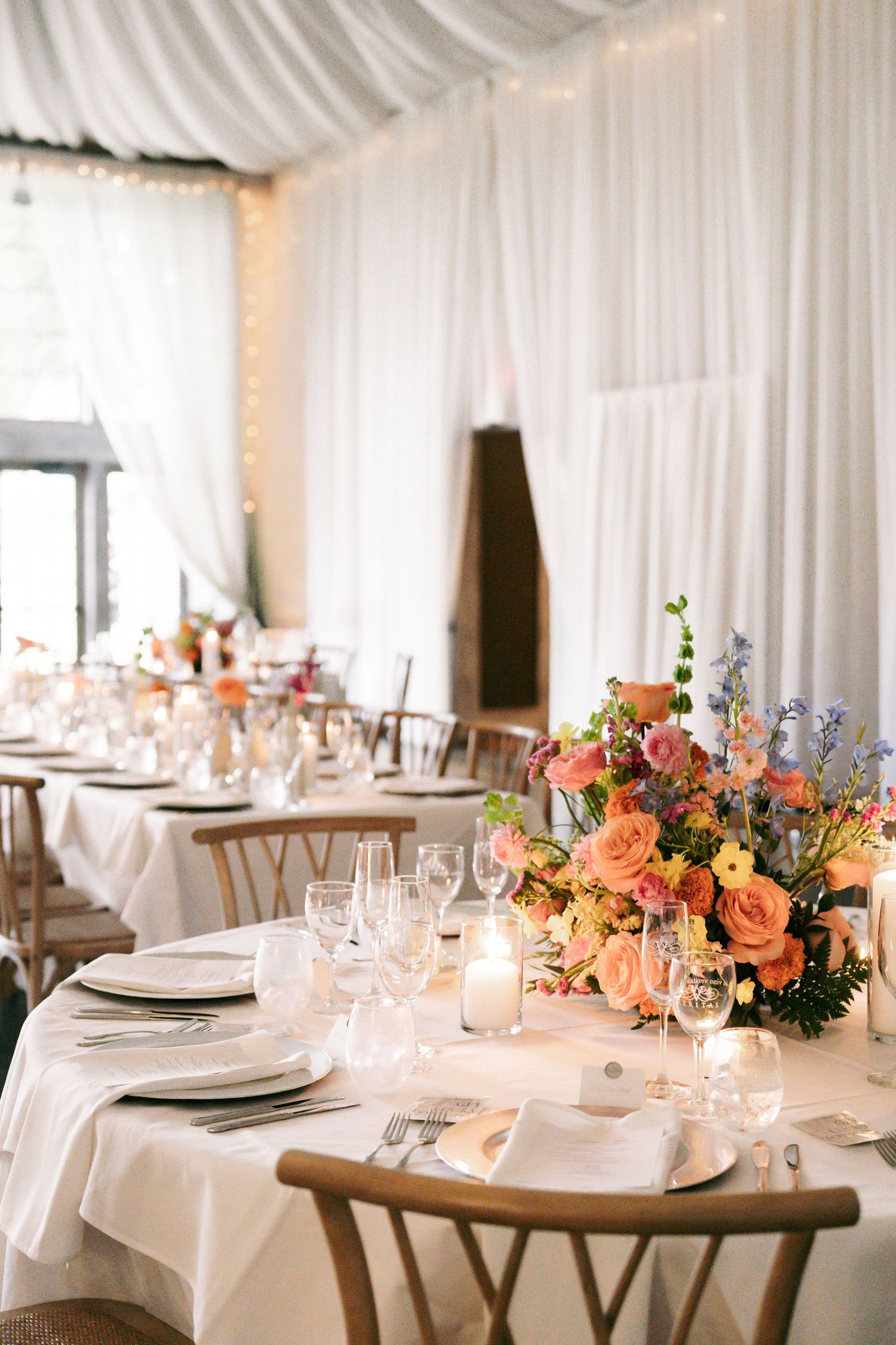 Elegant wedding reception table with colorful floral centerpiece, white linens, and glowing candles.