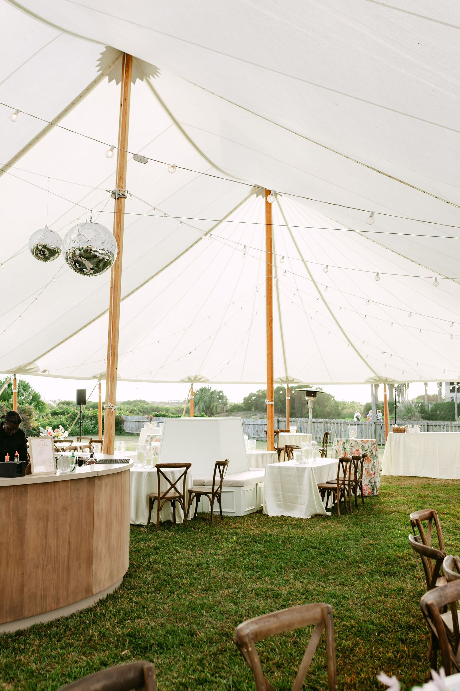 Elegant sailcloth wedding reception tent with disco balls, string lights, wooden chairs, and white draped tables.