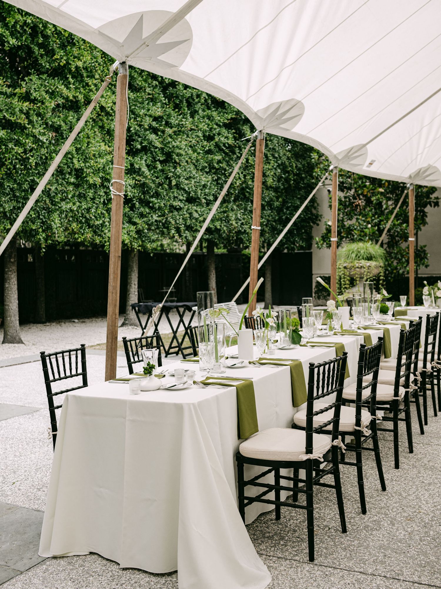 Elegant outdoor wedding reception under a white tent with long tables, green napkins, and black Chiavari chairs.