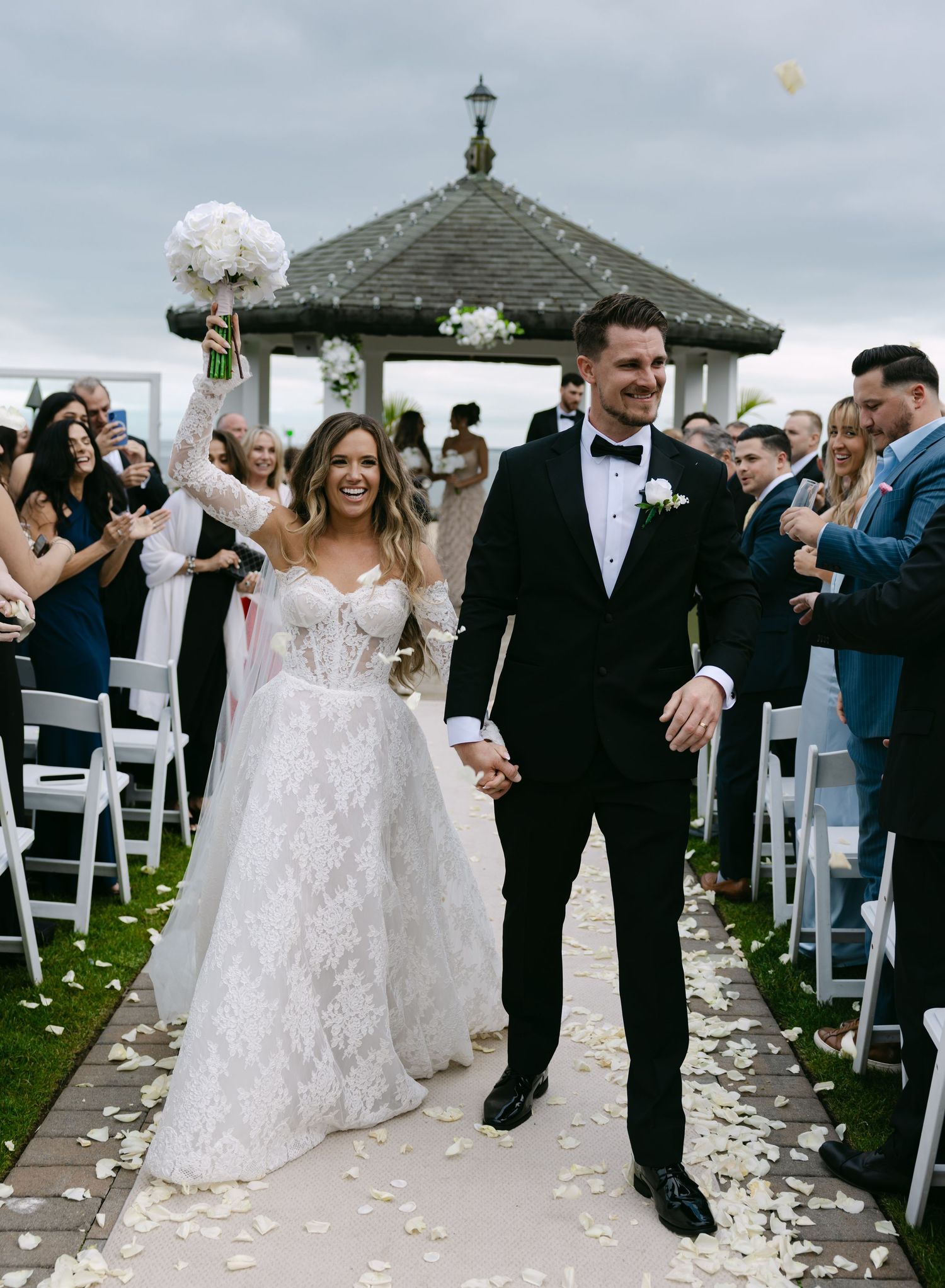 Wedding couple walking down aisle after ceremony with white chairs and flower petals.