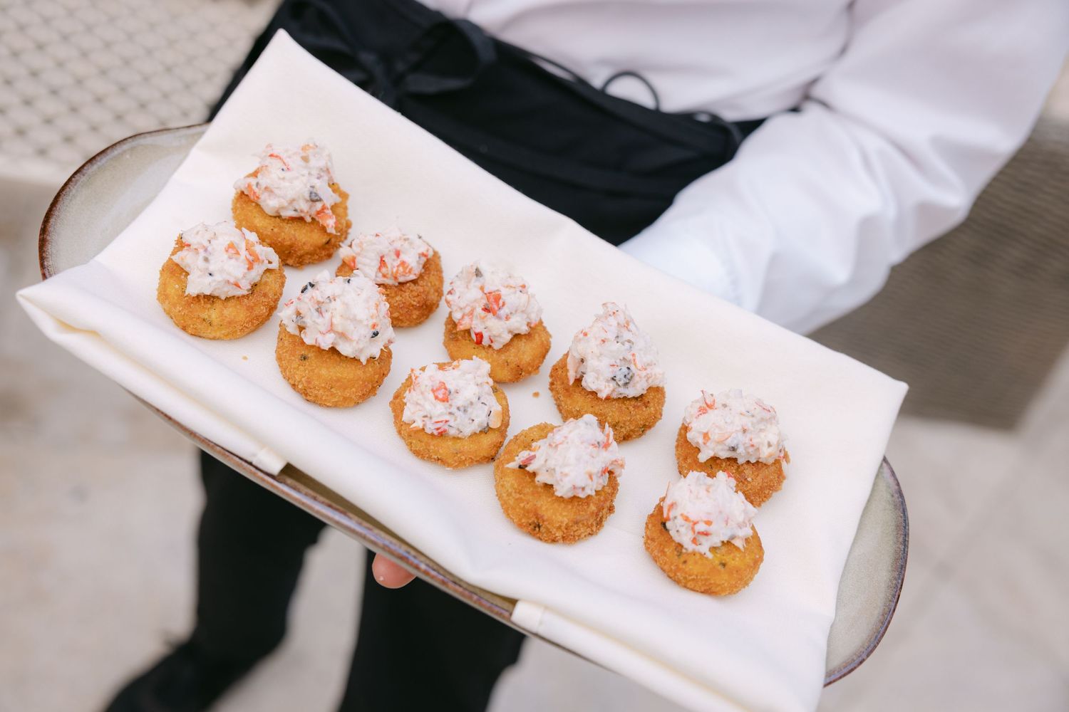 Tray of powdered sugar topped cream puffs being served at an elegant event.