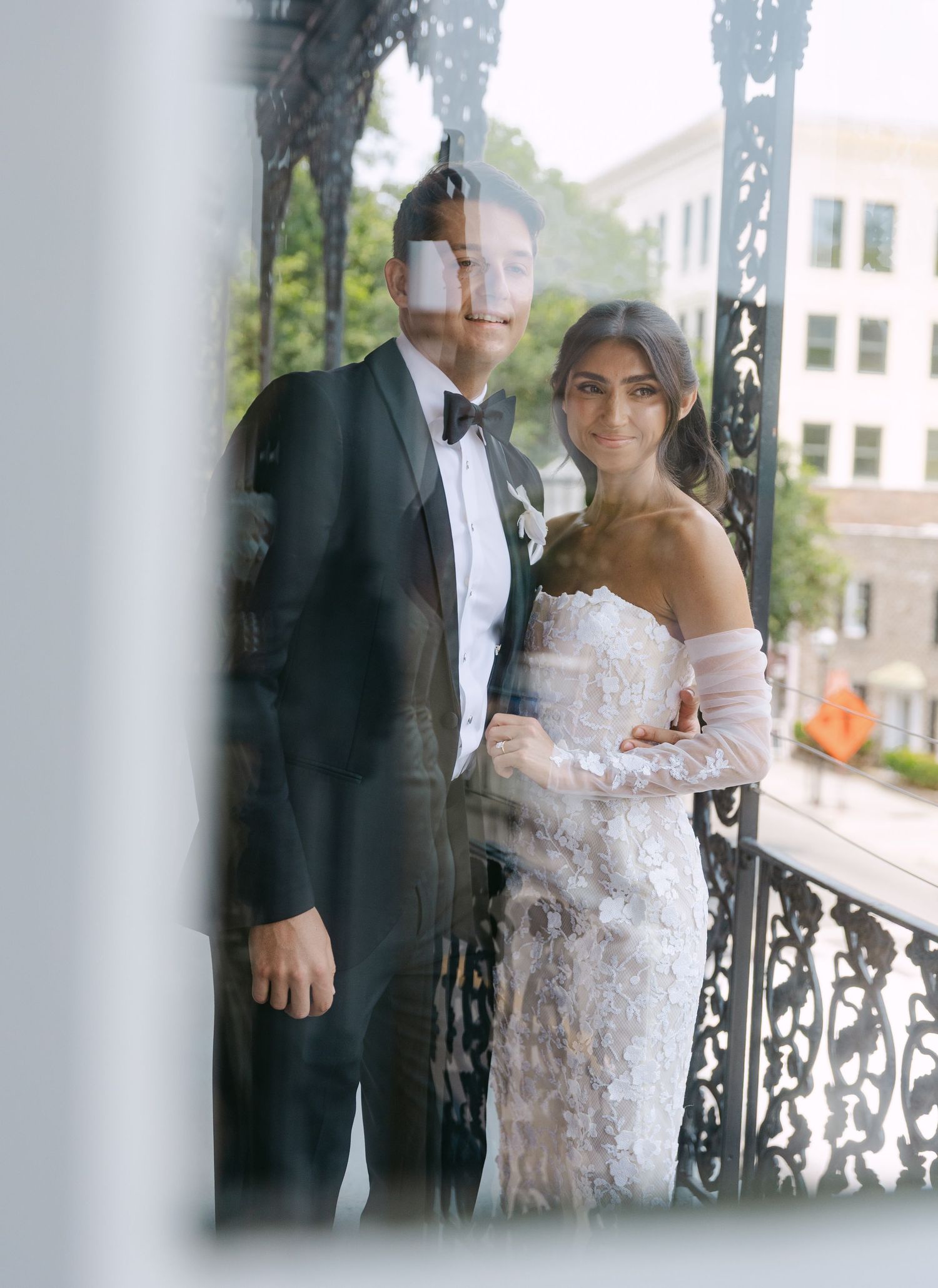 Wedding couple photographed through glass on a balcony with ornate ironwork.