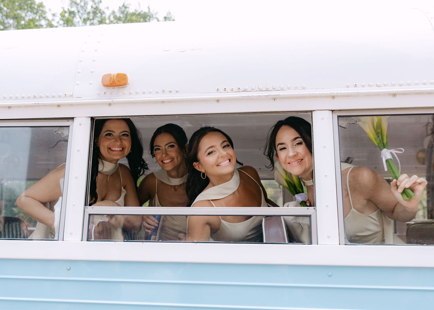 Bridesmaids peek out and pose through windows of a white limousine.