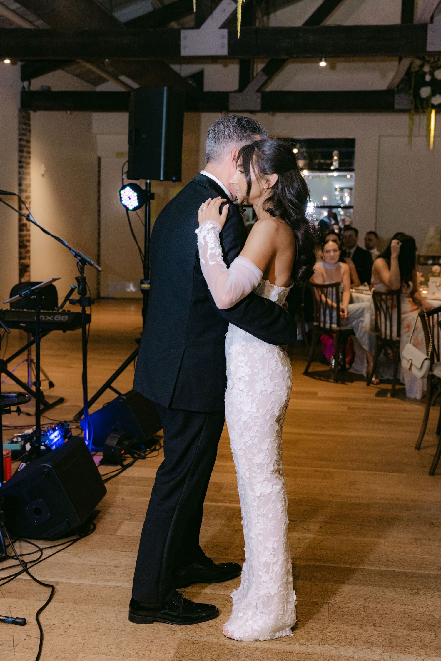 Newlyweds share first dance in rustic venue with hardwood floors and high ceilings.