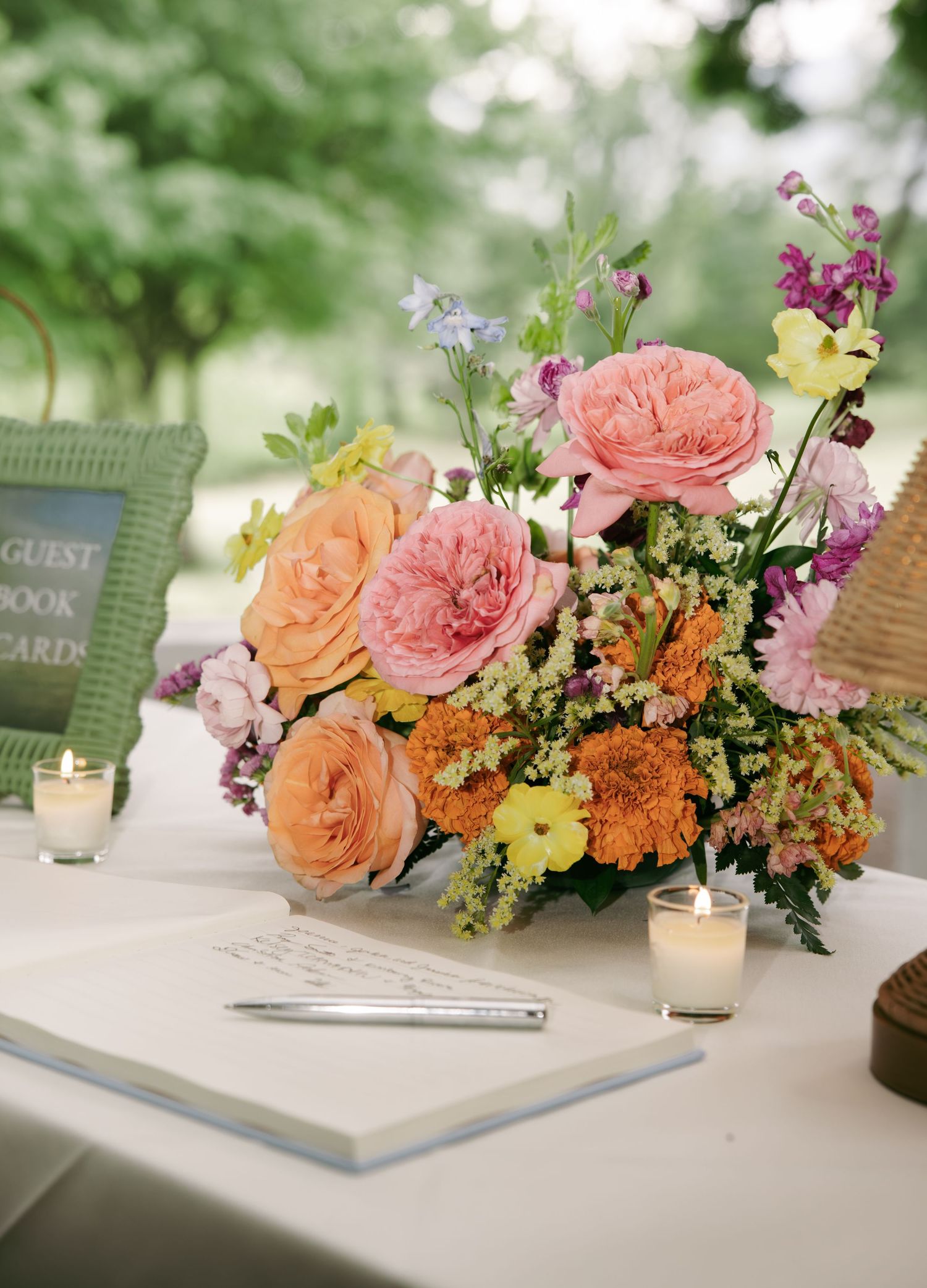 Colorful wedding guest book table with pink and orange floral arrangement, open registry book, and candles.