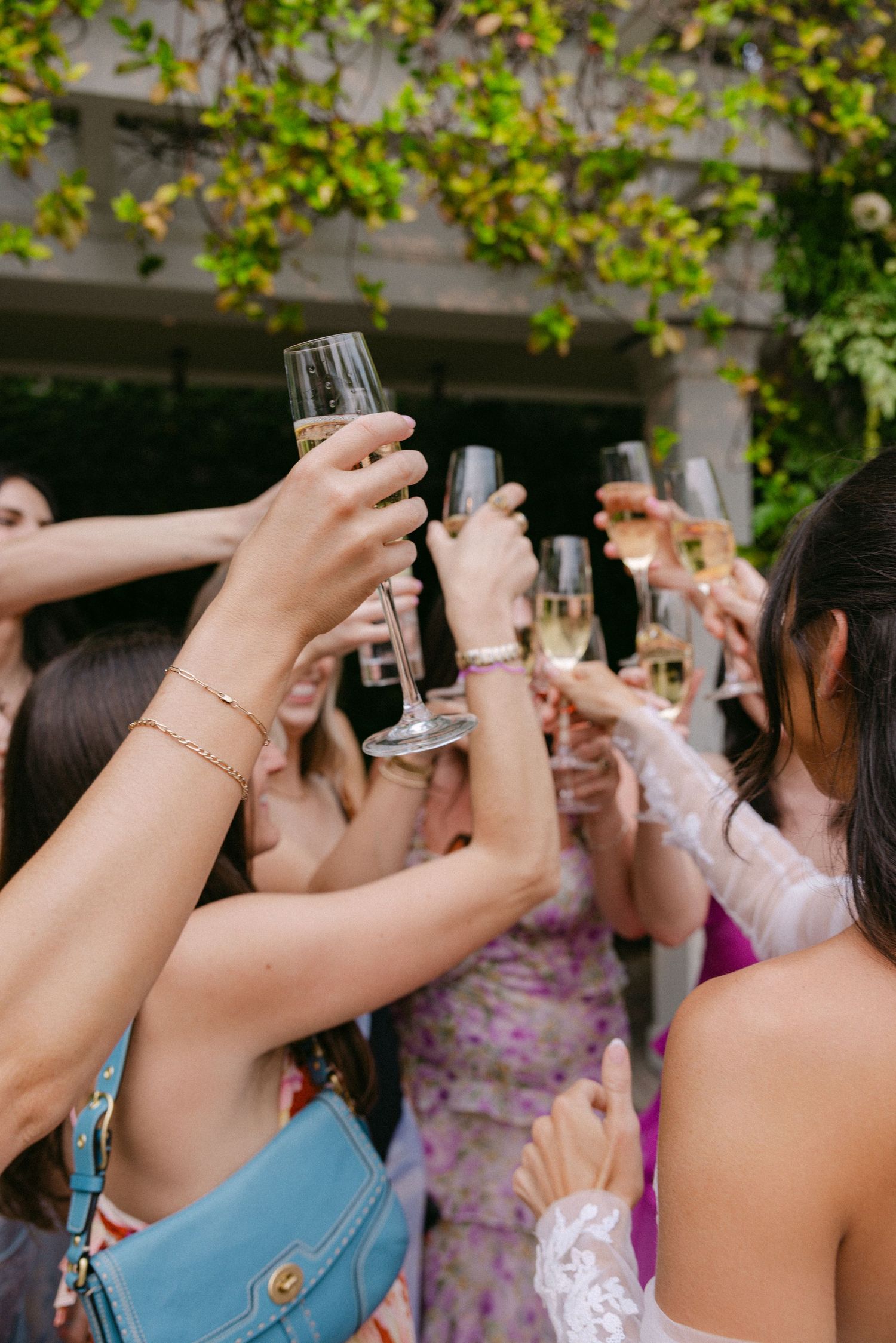 Wedding guests raise glasses in a toast during an outdoor garden celebration.