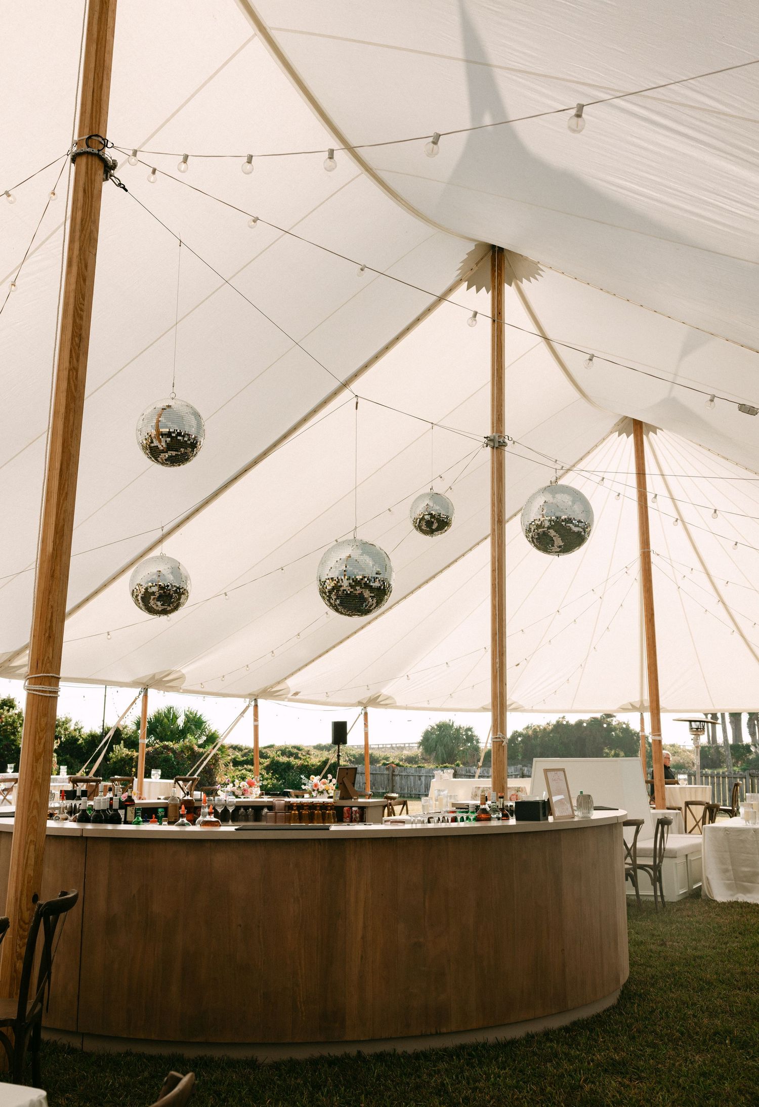 Elegant wedding tent with white canopy, wooden circular bar, and hanging disco balls creating a festive atmosphere.